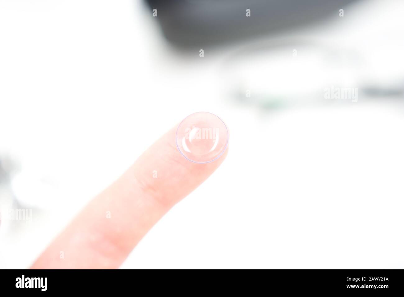 Hand mit Kontaktlinse, die in die Augen eingesetzt werden kann. Im Hintergrund sichtbare Brille, Tropfen und Hüllen Stockfoto