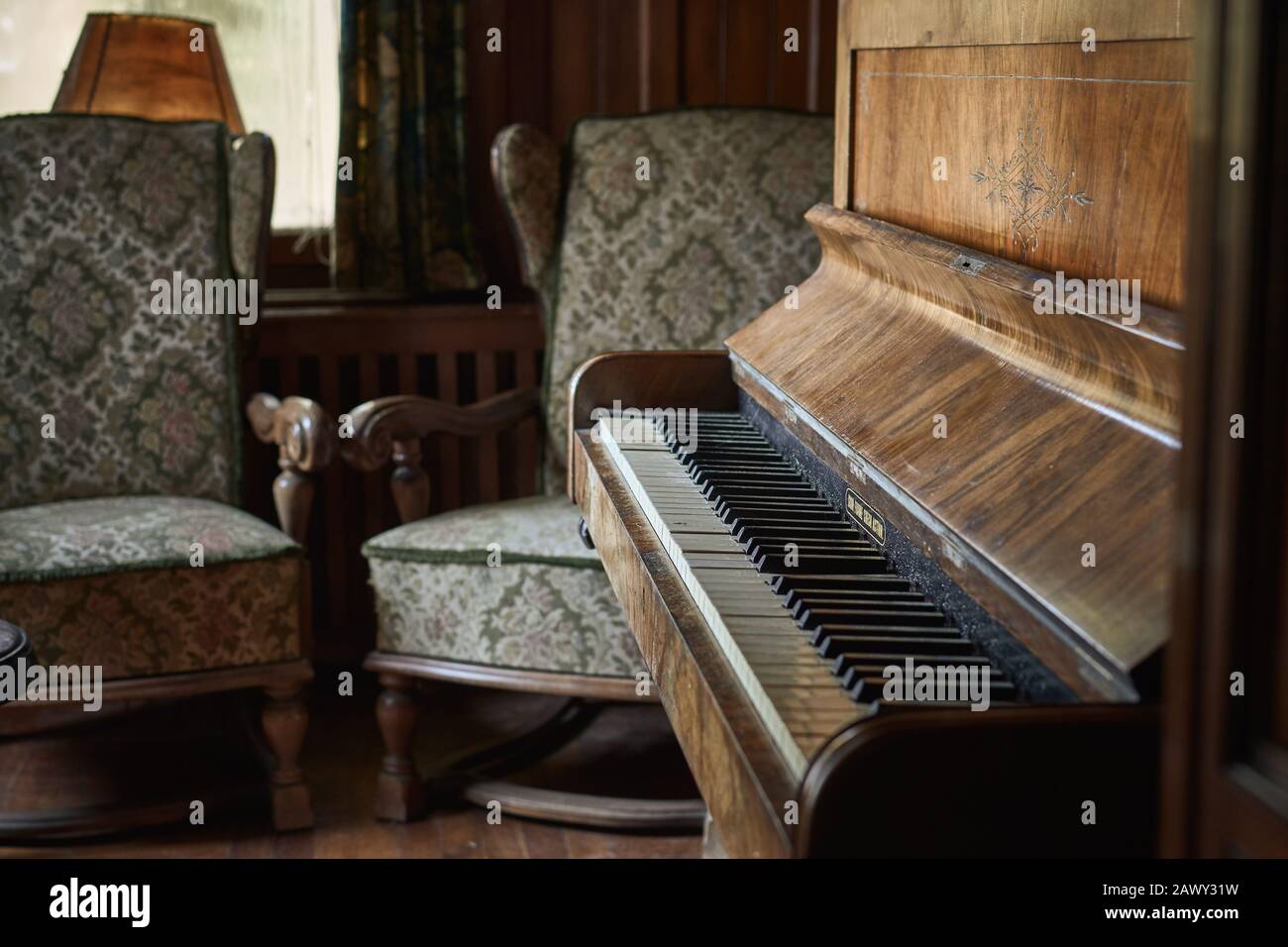 Vintage-Zimmer mit luxuriösem Klavier auf rustikalem und Holzboden und zwei alten Sesseln vor einem schmutzigen Fenster Stockfoto