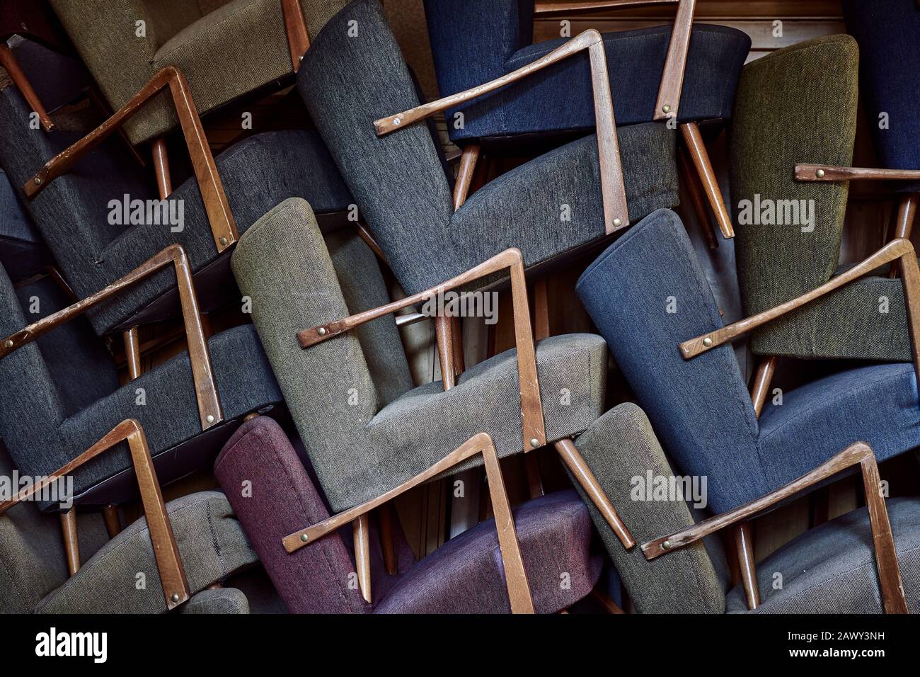 Vintage-Sessel stapelten sich. Vollformat und Nahaufnahme vieler farbenfroher, mit Stoff bedeckter und gepolsterter Stühle mit gestapelten Holzgriffen Stockfoto