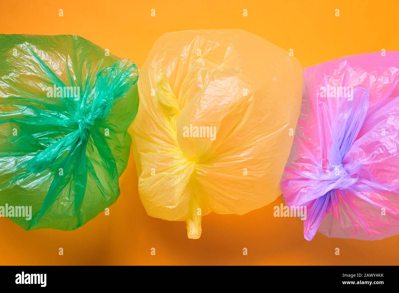 Horizontal von oben konzeptionell aus drei mehrfarbigen Plastiktüten voller Luft auf orangefarbenem Hintergrund Stockfoto