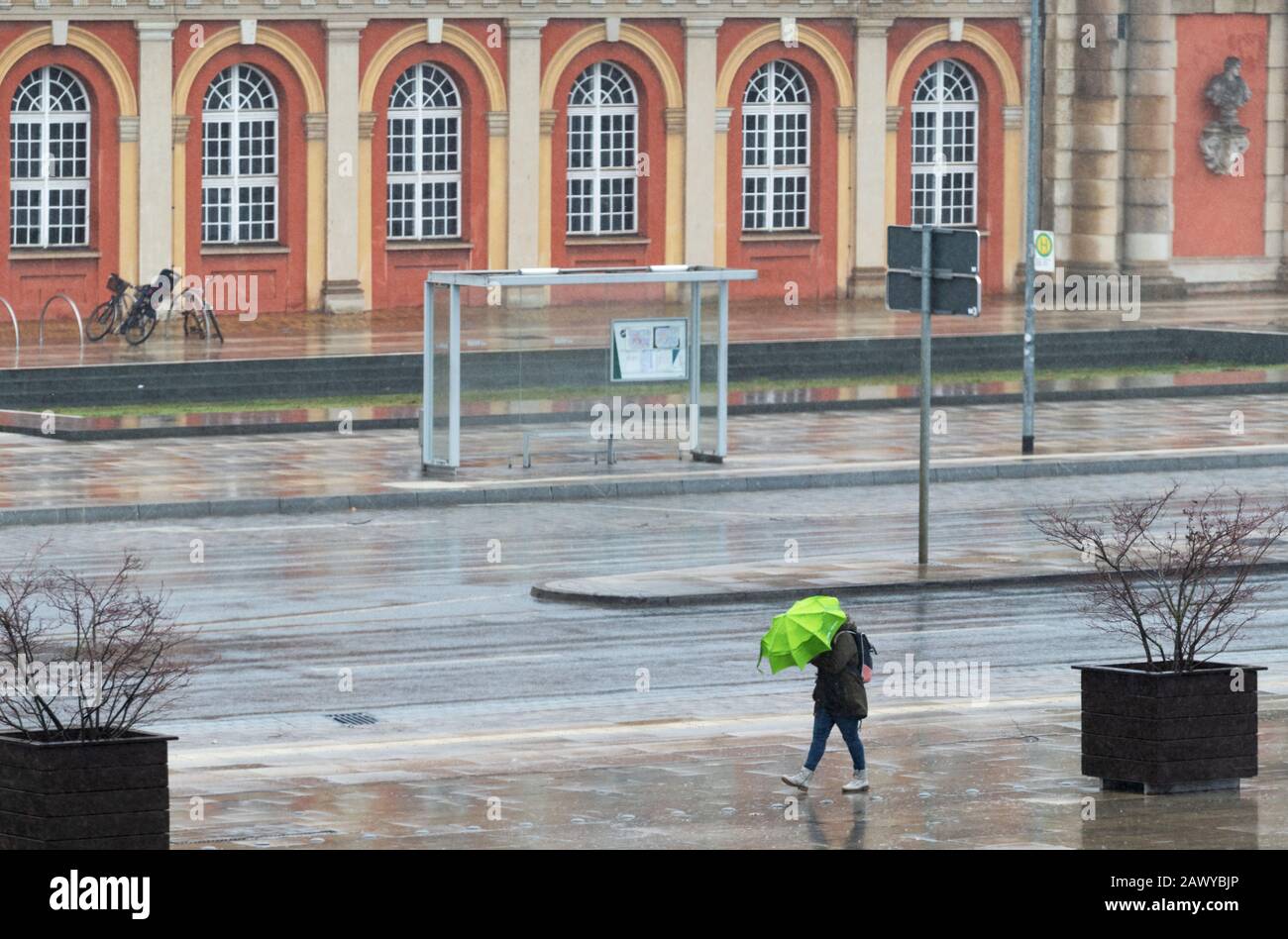 Potsdam, Deutschland. Februar 2020. Eine Frau mit grünem Regenschirm schützt sich vor Regen und Wind vor der Kulisse des Filmmuseum, nachdem der Sturm 'Sabine' Deutschland in der Nacht getroffen hat. Kredit: Soeren Stache / dpa-Zentralbild / ZB / dpa / Alamy Live News Stockfoto