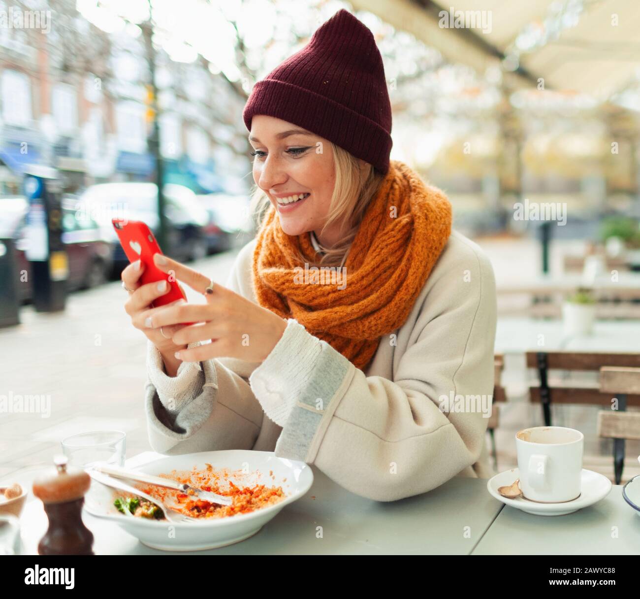 Lächelnde junge Frau mit Smartphone zum Mittagessen im Straßencafé im Herbst Stockfoto