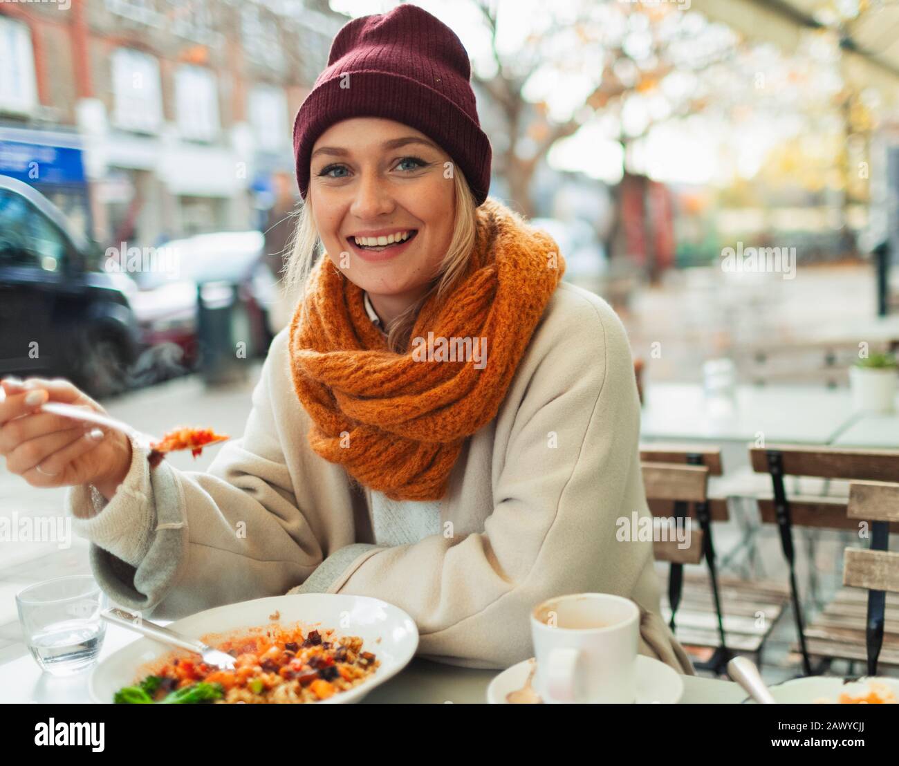 Portrait lächelnde Frau, die im Herbst im Straßencafé zu Mittag essen Stockfoto