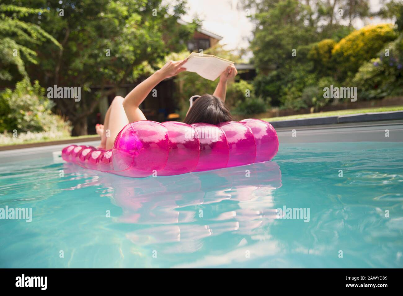 Frau liest Buch über aufblasbares Floß im sonnigen Sommer-Swimmingpool Stockfoto