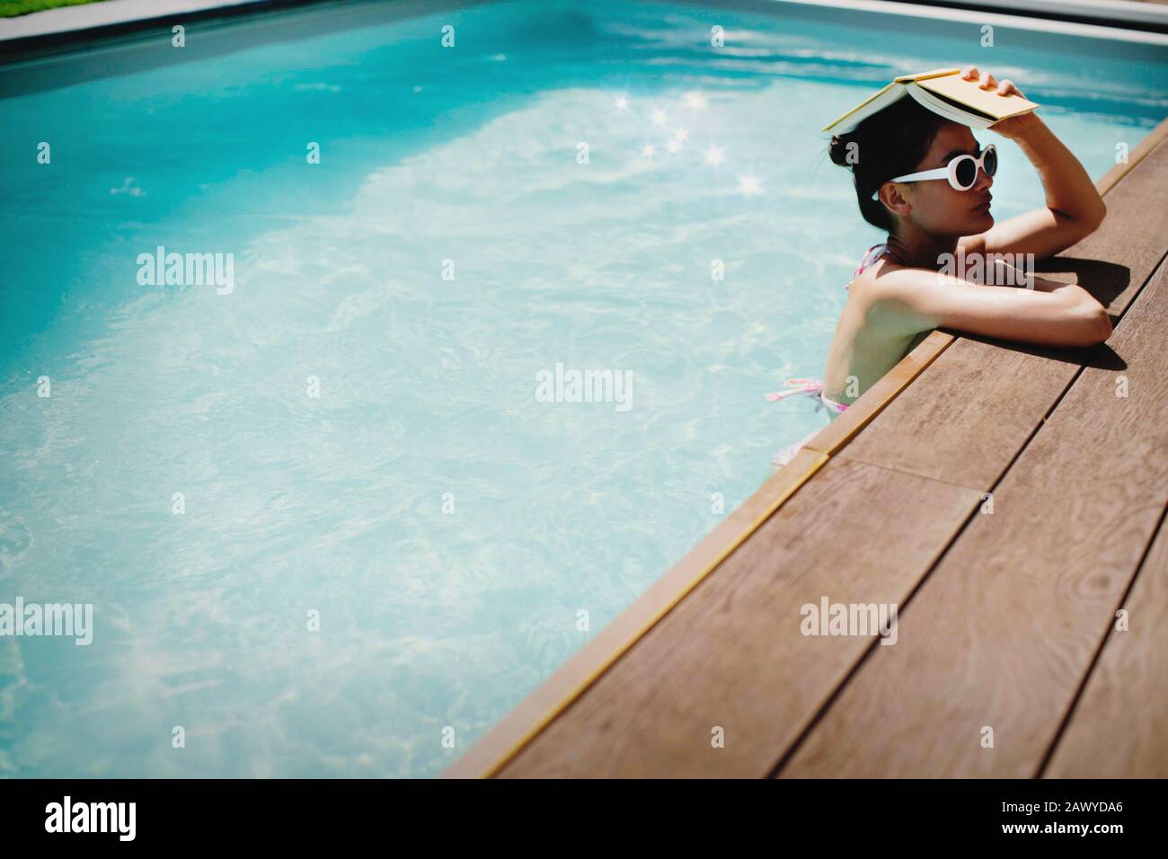 Frau, die im sonnigen Sommer-Swimmingpool buchen kann Stockfoto