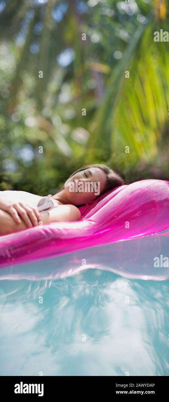 Ruhige Frau, entspannend, schlafend auf einem aufblasbaren Floß im sonnigen Schwimmbad Stockfoto