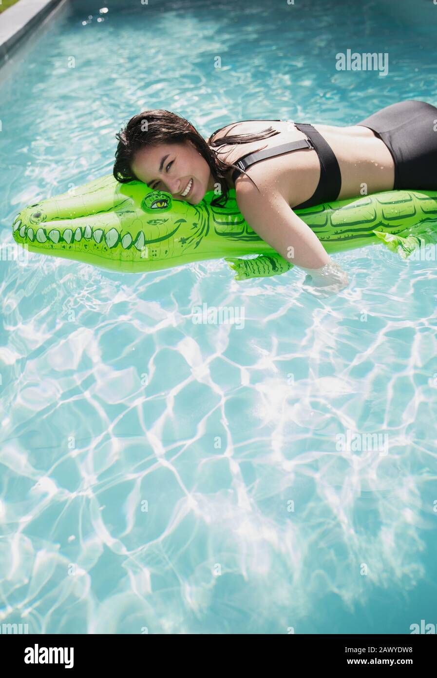 Portrait unbeschwerte Frau schwimmt auf aufblasbarem Krokodilfloß im sonnigen Sommer-Schwimmbad Stockfoto