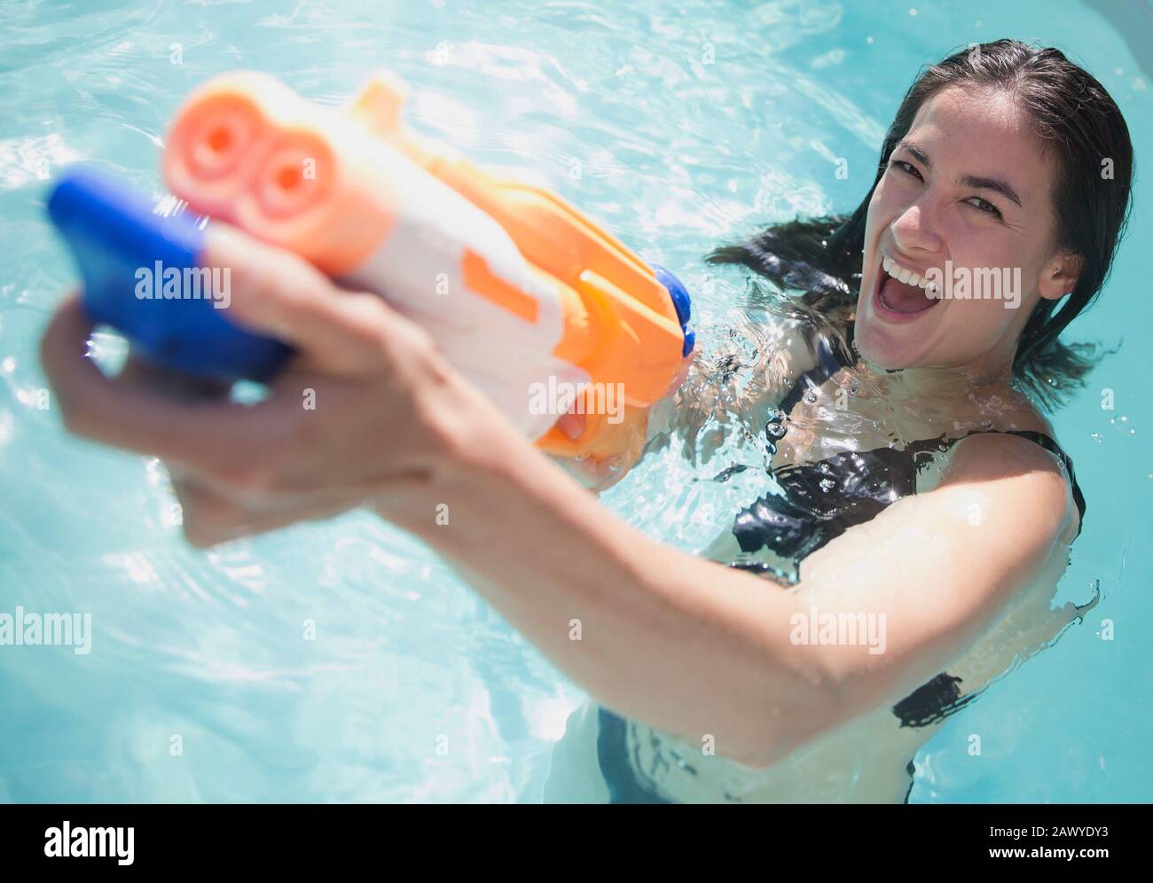 Portrait verspielte Frau mit Hauspistole im sonnigen Schwimmbad Stockfoto
