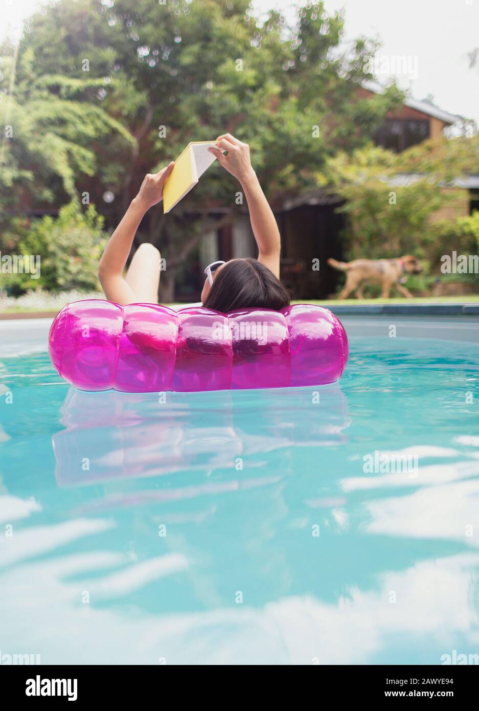 Frau entspannend, Lesebuch über aufblasbares Floß im sonnigen Sommer-Swimmingpool Stockfoto