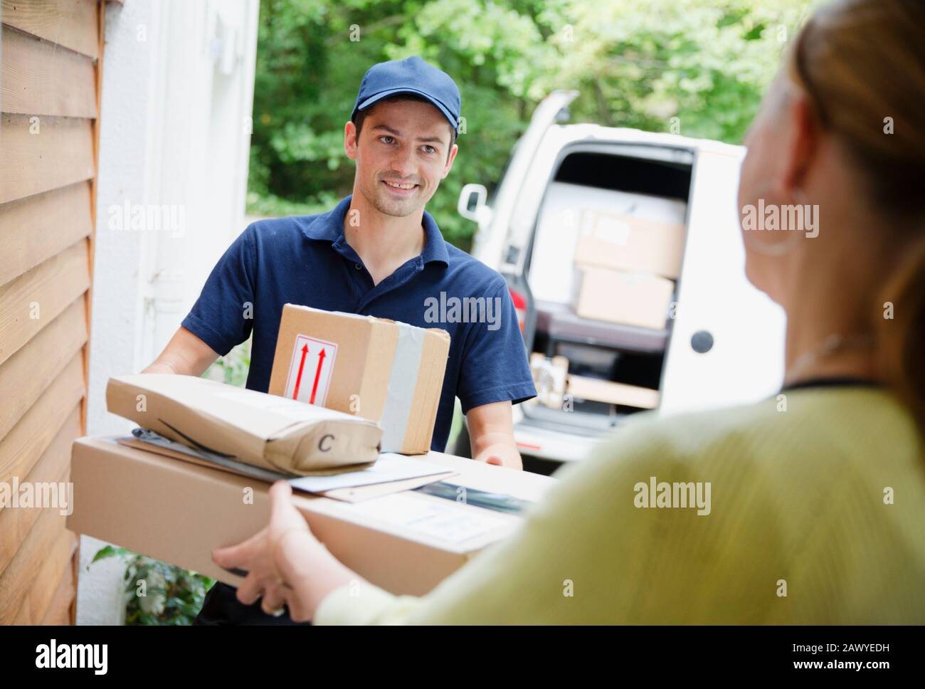 Der Lieferer liefert die Pakete an die Frau vor der Tür Stockfoto