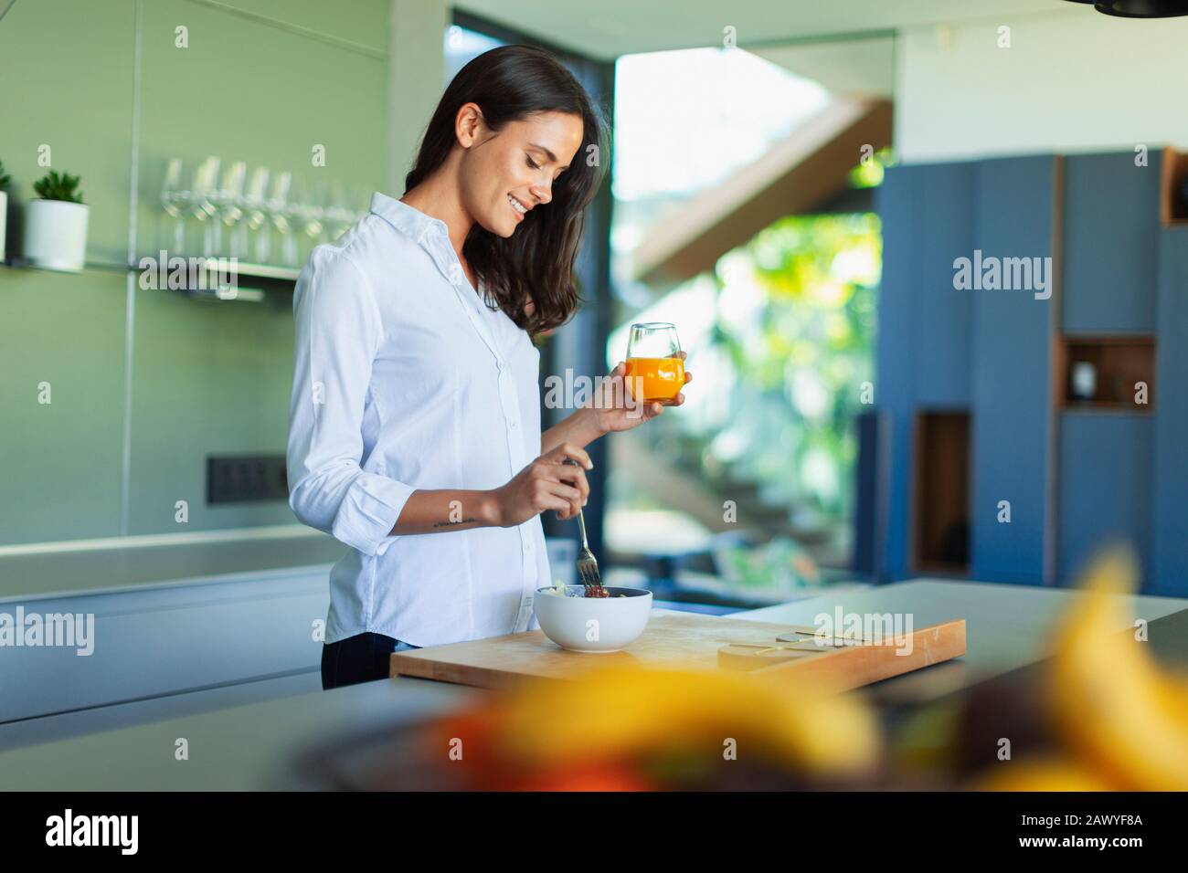 Lächelnde Frau trinkt Saft und isst Obst in der Küche Stockfoto