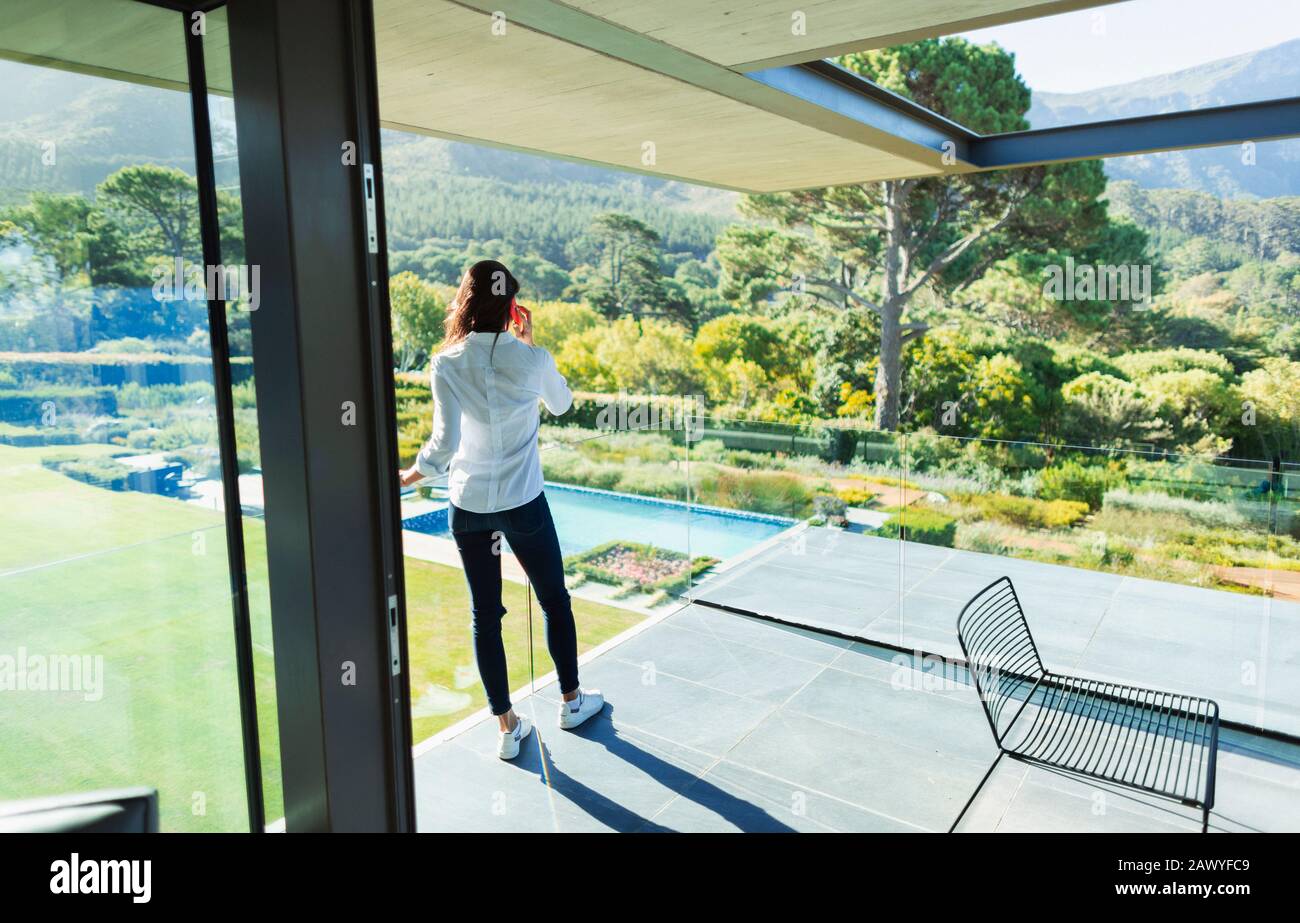 Frau spricht auf einem sonnigen Luxus-Balkon mit Blick auf das Smartphone Stockfoto