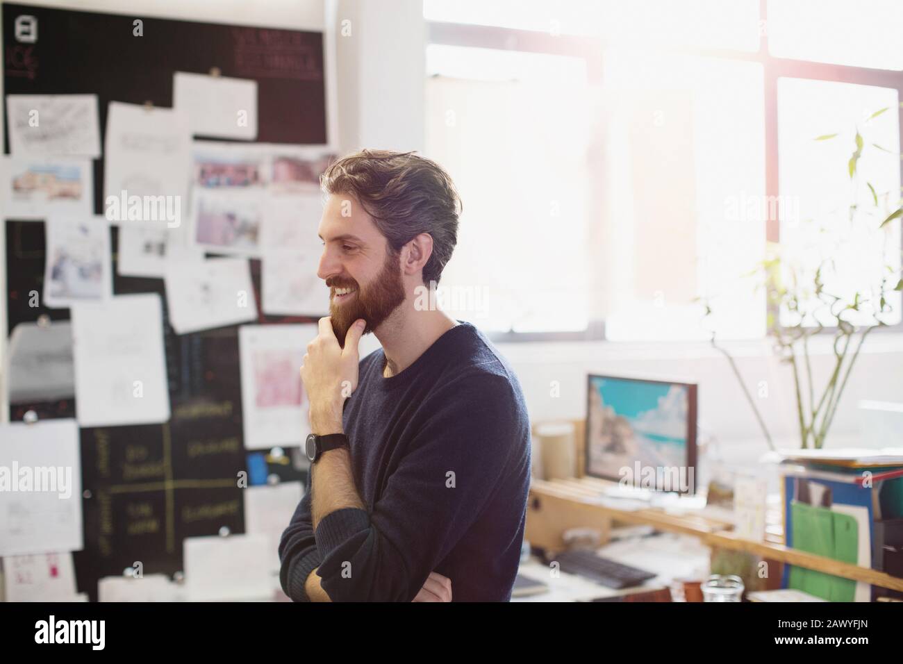 Fröhlicher kreativer Geschäftsmann reibt Bart im Büro Stockfoto