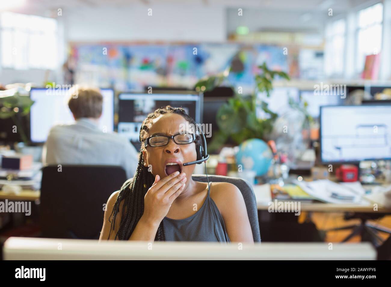 Müde Geschäftsfrau mit Headset gähnelt am Computer im offenen Büro Stockfoto