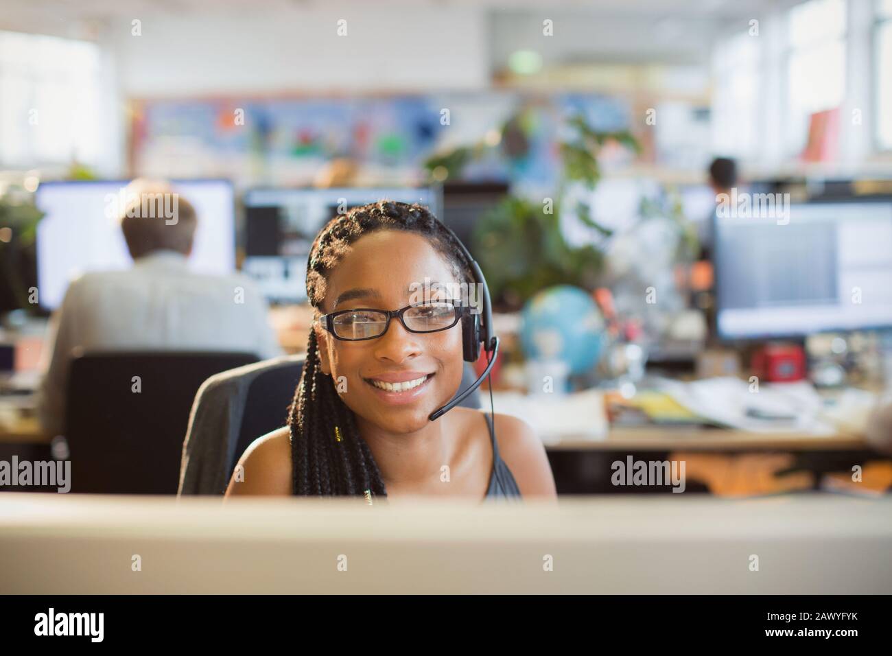 Portrait selbstbewusste Geschäftsfrau mit Headset, das am Computer in einem offenen Büro arbeitet Stockfoto