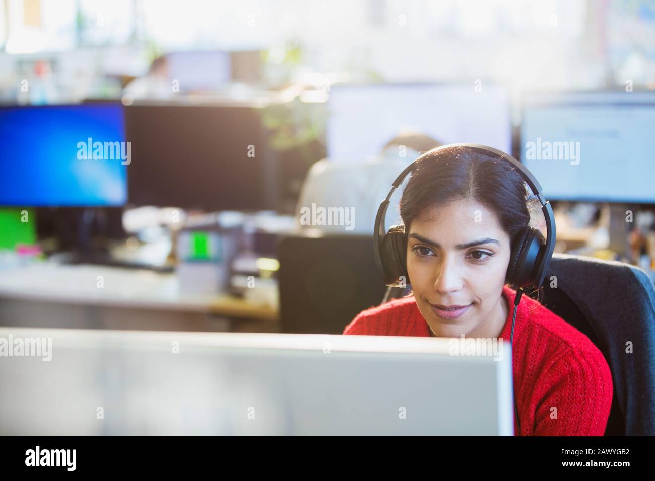 Geschäftsfrau mit Kopfhörern, die am Computer im Büro arbeiten Stockfoto