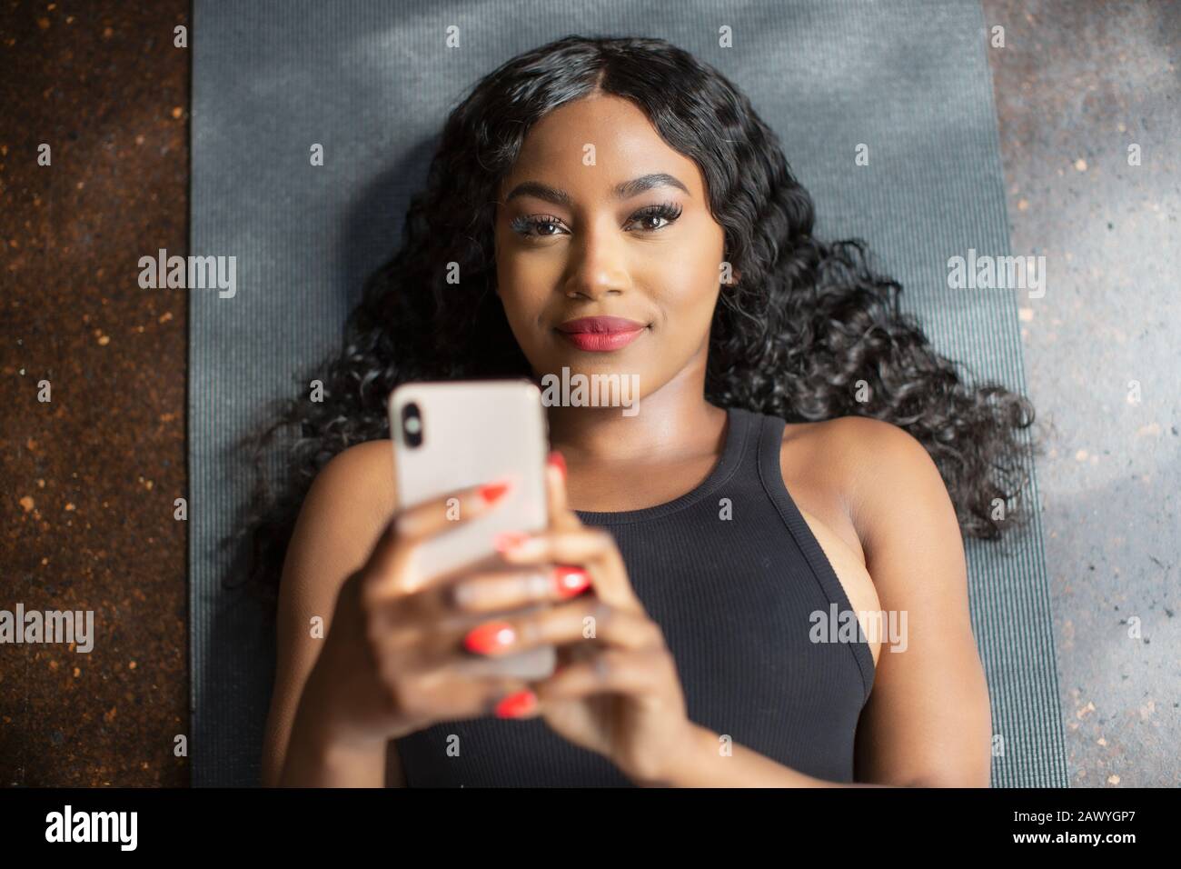Portrait selbstbewusste junge Frau mit Smartphone auf Yogamatte Stockfoto