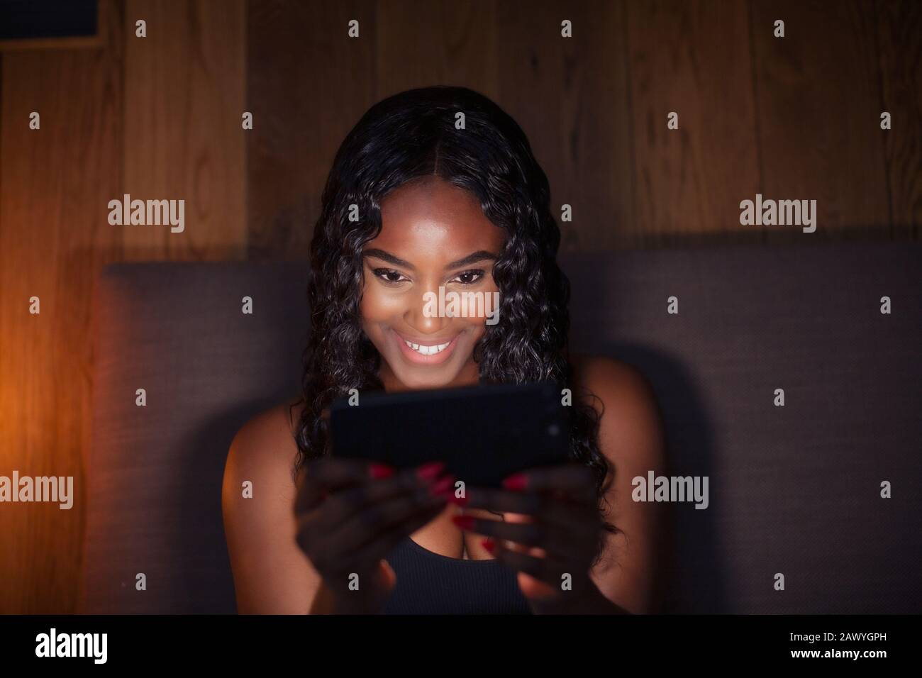 Glückliche junge Frau mit Smartphone im dunklen Schlafzimmer Stockfoto