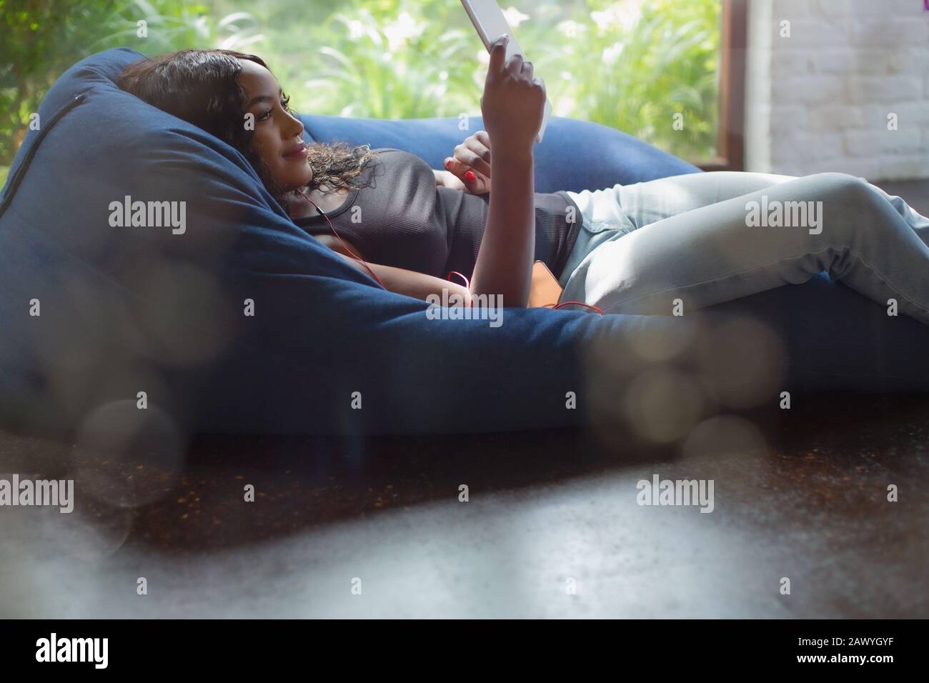 Junge Frau, die sich mit einem digitalen Tablett im Beansack-Stuhl entspannen kann Stockfoto