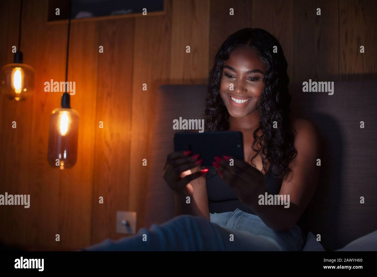Lächelnde junge Frau mit Smartphone im dunklen Schlafzimmer Stockfoto
