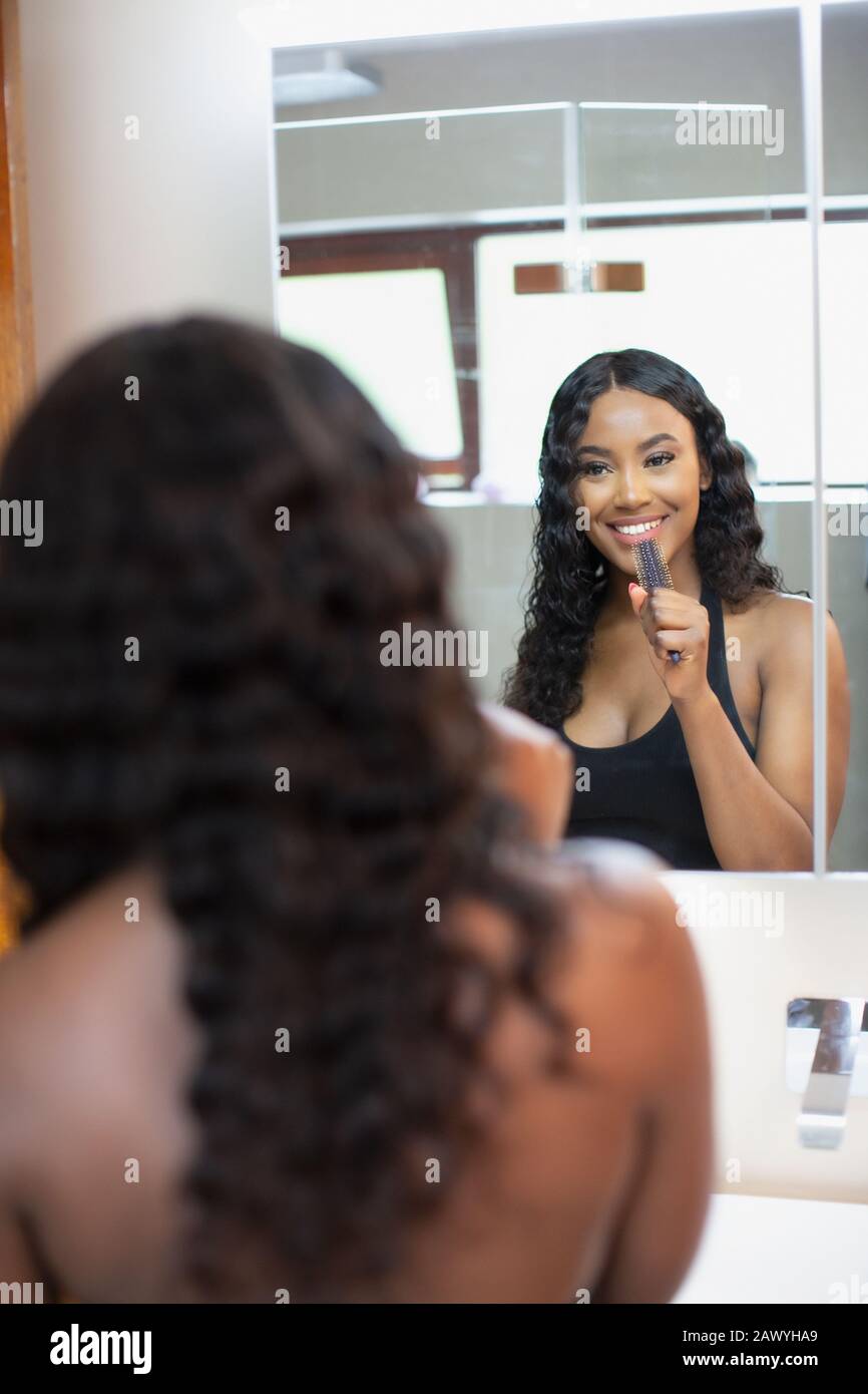Fröhliche junge Frau singt mit Haarbürste im Badezimmerspiegel Stockfoto