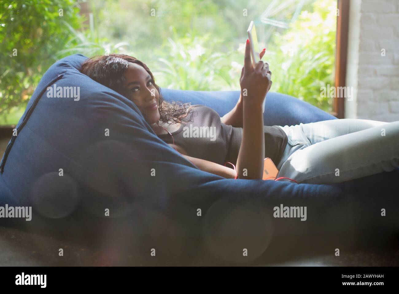 Portrait lächelnde junge Frau entspannend mit digitaler Tablette im Beanttasche Stuhl Stockfoto