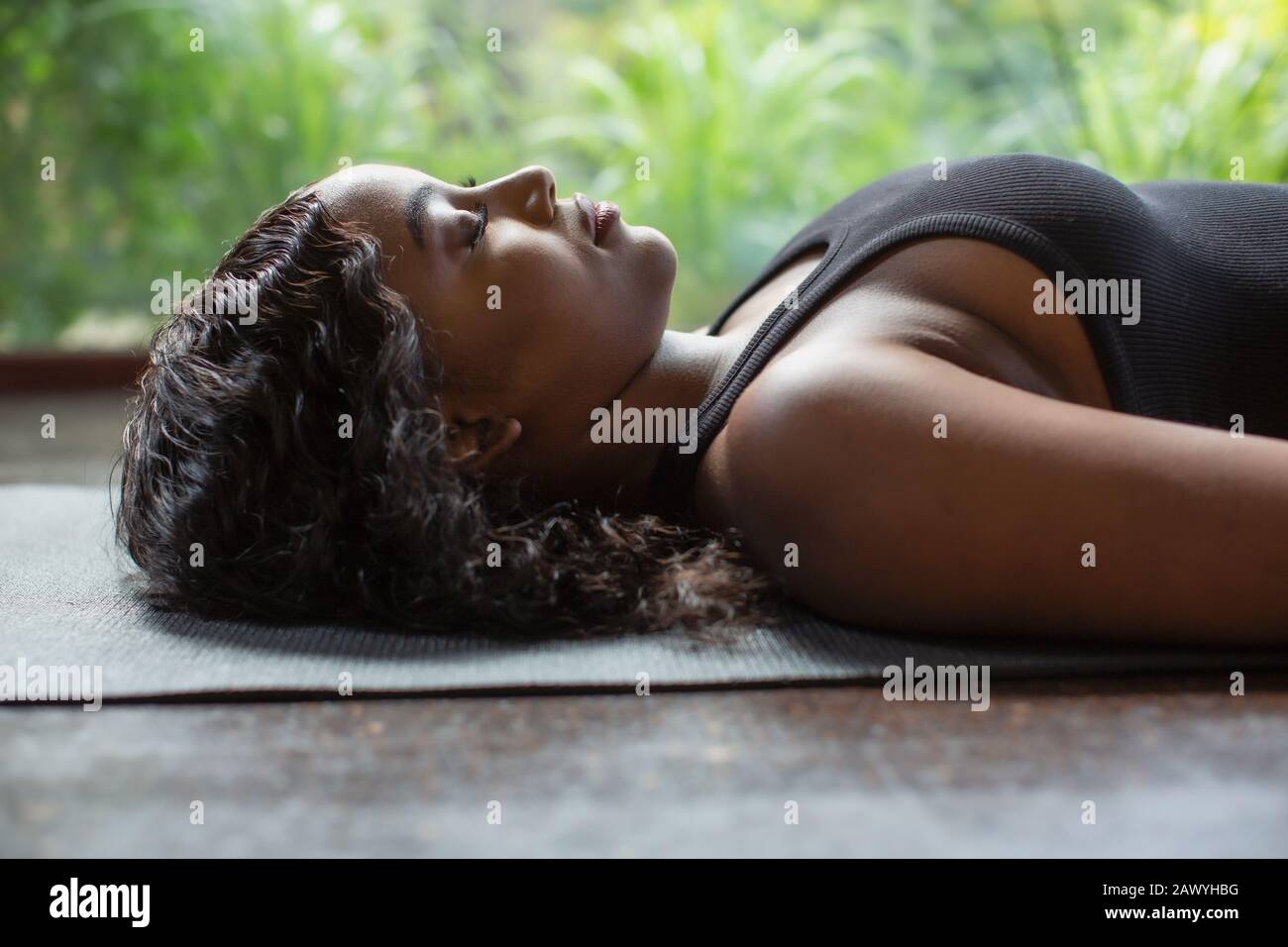 Heitere junge Frau, die in Leichenstellung auf Yogamatte legt Stockfoto