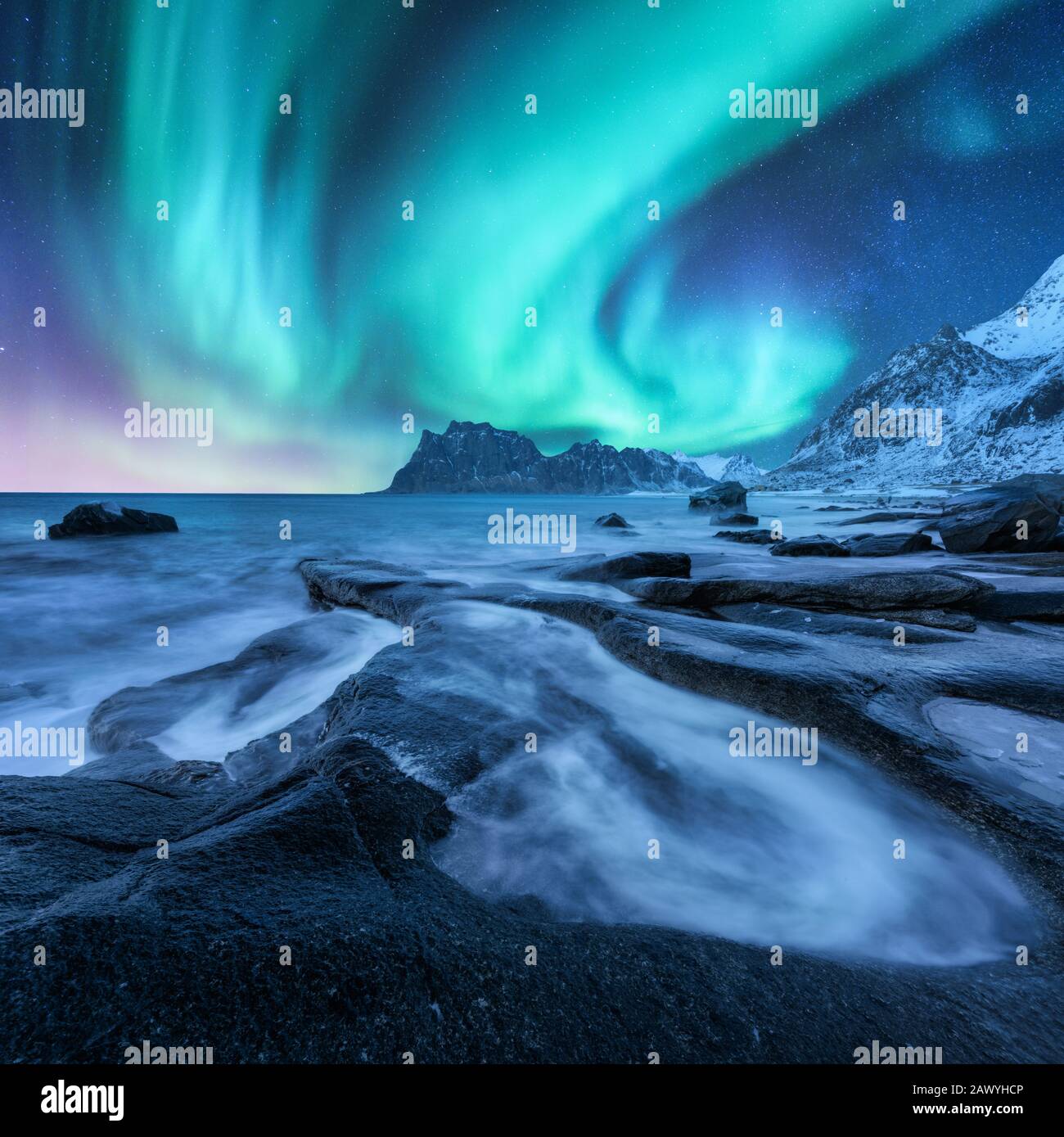 Aurora borealis, verschneite Berge und sandiger Strand mit Steinen Stockfoto