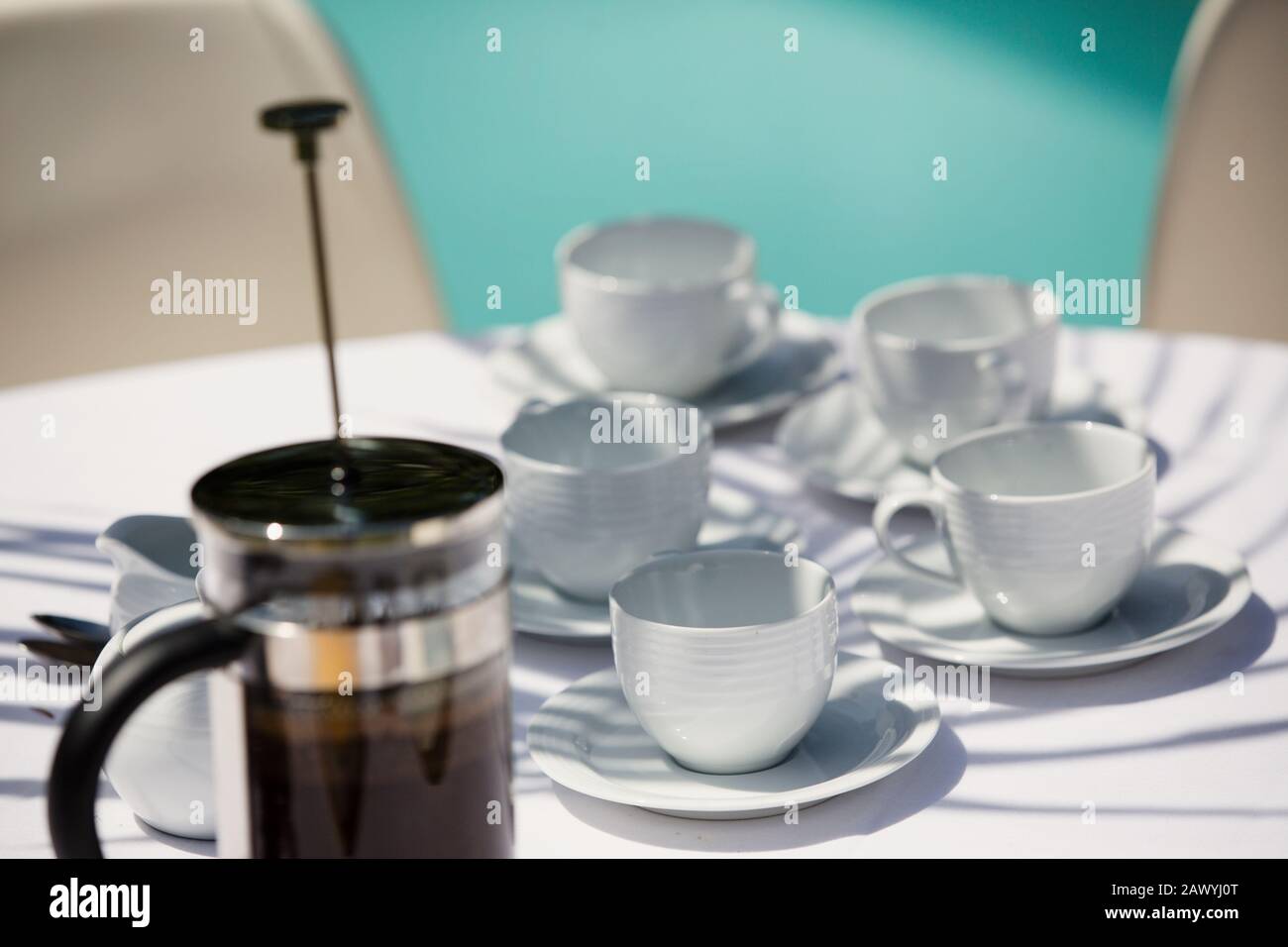 Französische Presse und Kaffeetassen auf einem sonnigen Terrassentisch Stockfoto