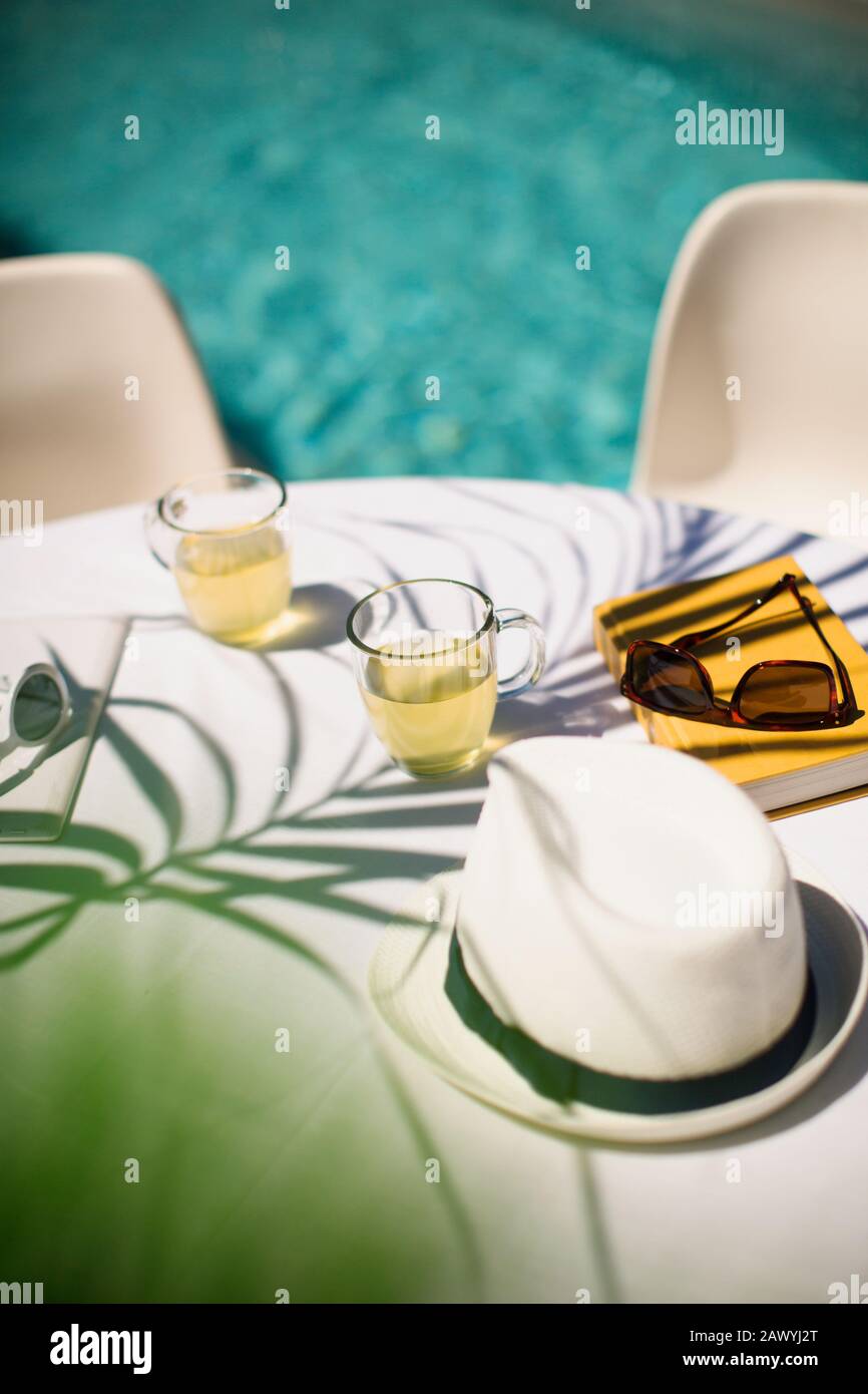 Tee- und Sonnenhut auf dem sonnigen Sommertisch auf der Terrasse am Pool Stockfoto