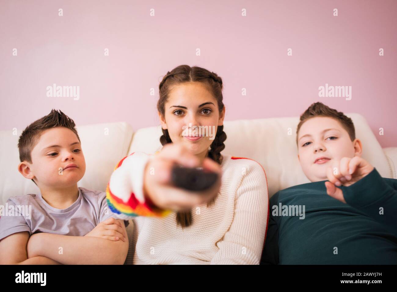 Portrait selbstbewusstes Mädchen mit Fernbedienung Fernsehen mit Brüdern Stockfoto