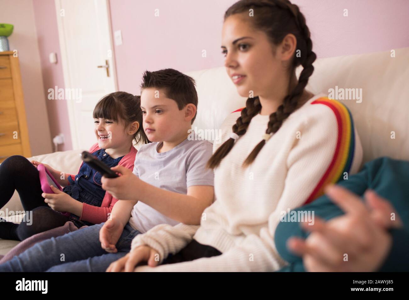 Junge mit Down-Syndrom Fernsehen mit Geschwistern auf dem Sofa Stockfoto