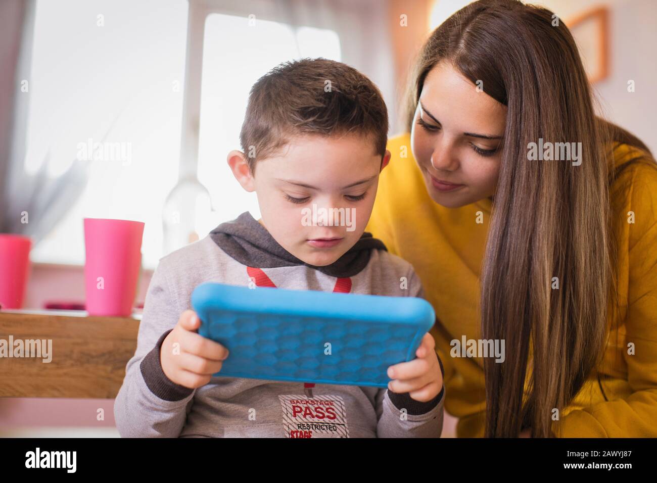Mädchen beobachtet Bruder mit Down-Syndrom mit digitalem Tablet Stockfoto