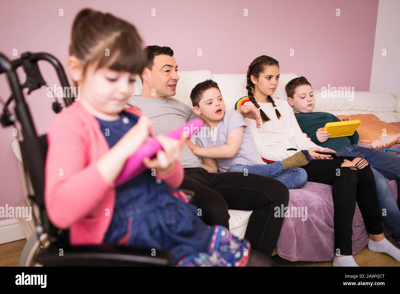 Familie mit Kind Im Down-Syndrom, die auf dem Sofa im Wohnzimmer Fernsehen Stockfoto