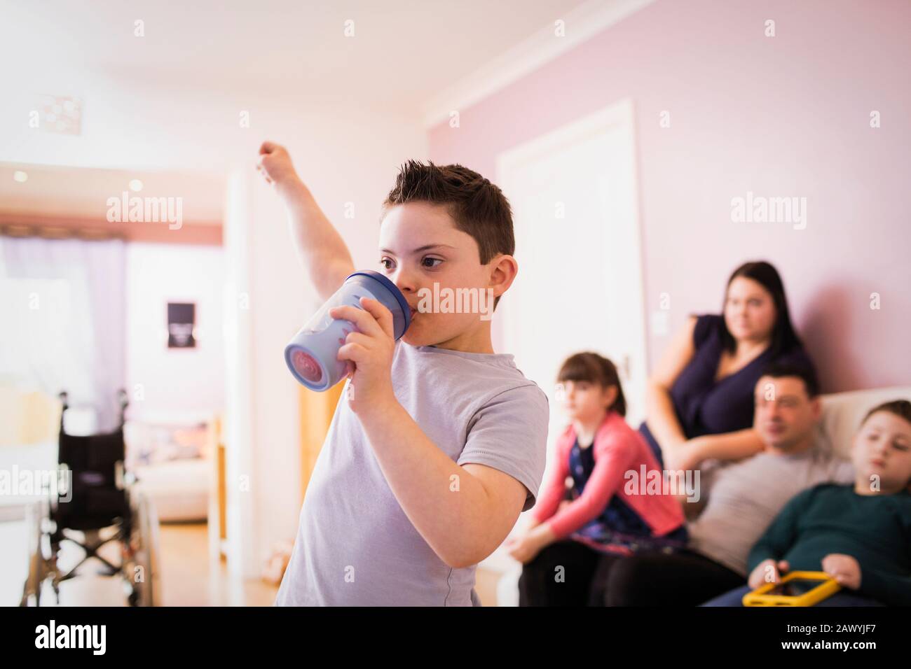 Junge mit Down-Syndrom im Wohnzimmer trinken und jubeln Stockfoto