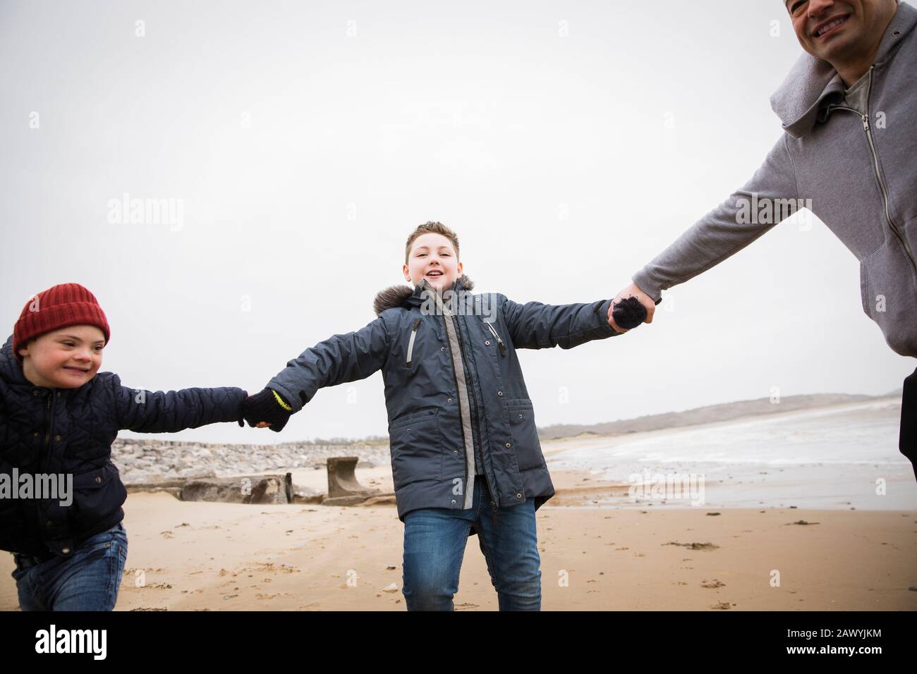 Verspielter Vater und seine Söhne halten sich am Winter-Ozean-Strand Stockfoto