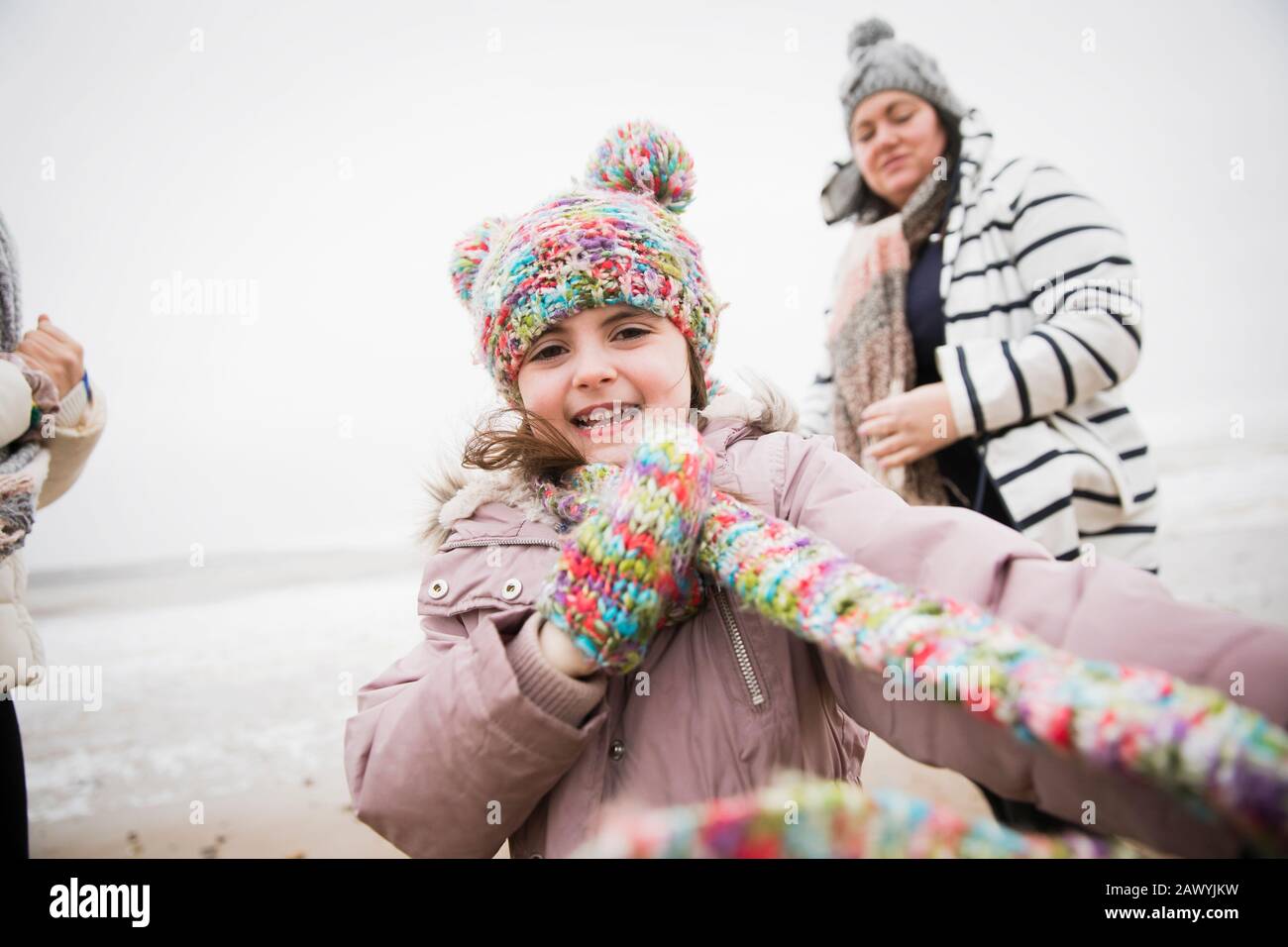 Portrait fröhliches, sorgloses Mädchen in warmer Kleidung am Winterstrand Stockfoto
