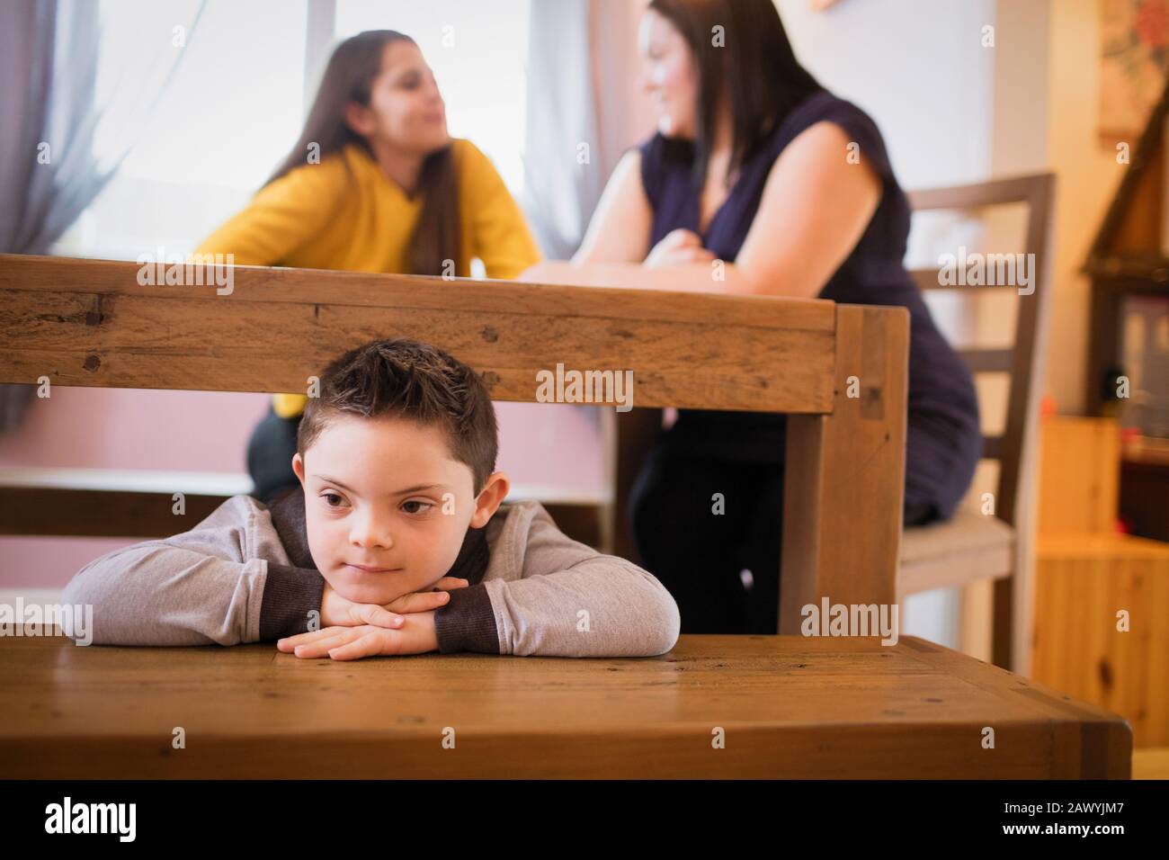 Junge mit Down-Syndrom, der unter dem Esstisch spielt Stockfoto