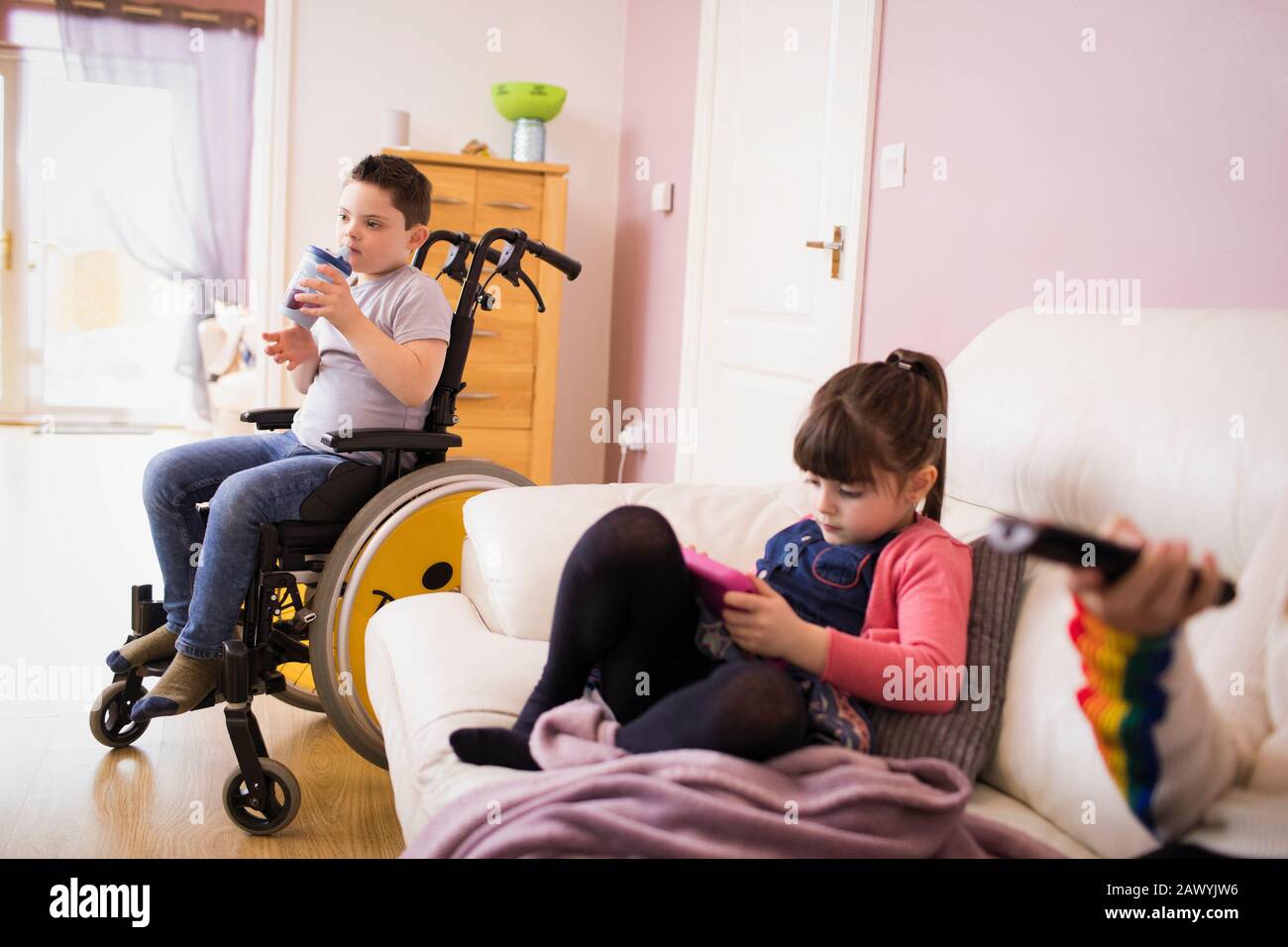 Junge mit Down-Syndrom im Rollstuhl und Schwester im Wohnzimmer Stockfoto