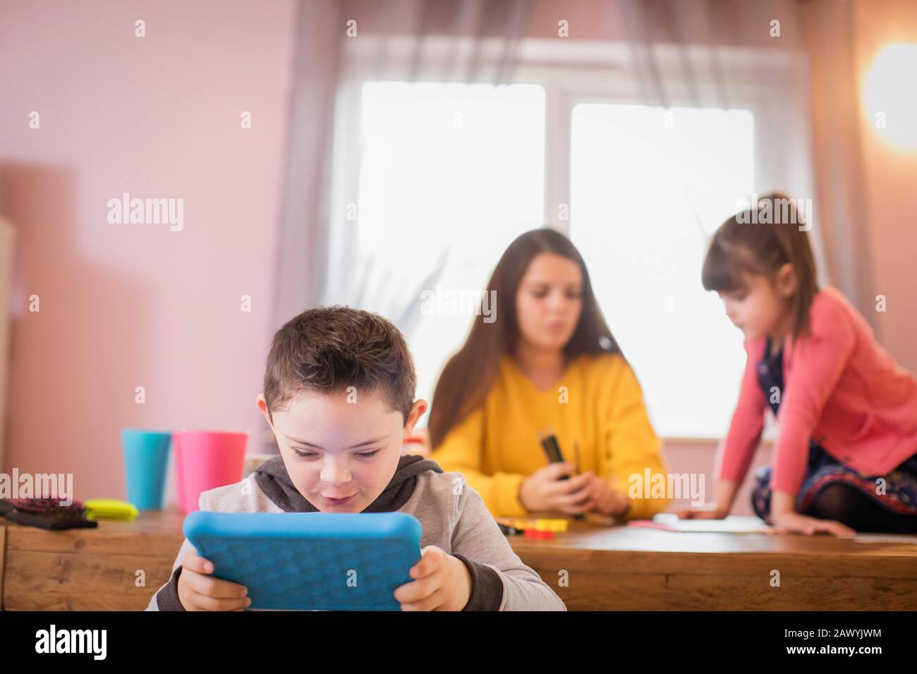 Junge mit Down-Syndrom mit digitalem Tablet am Esstisch Stockfoto