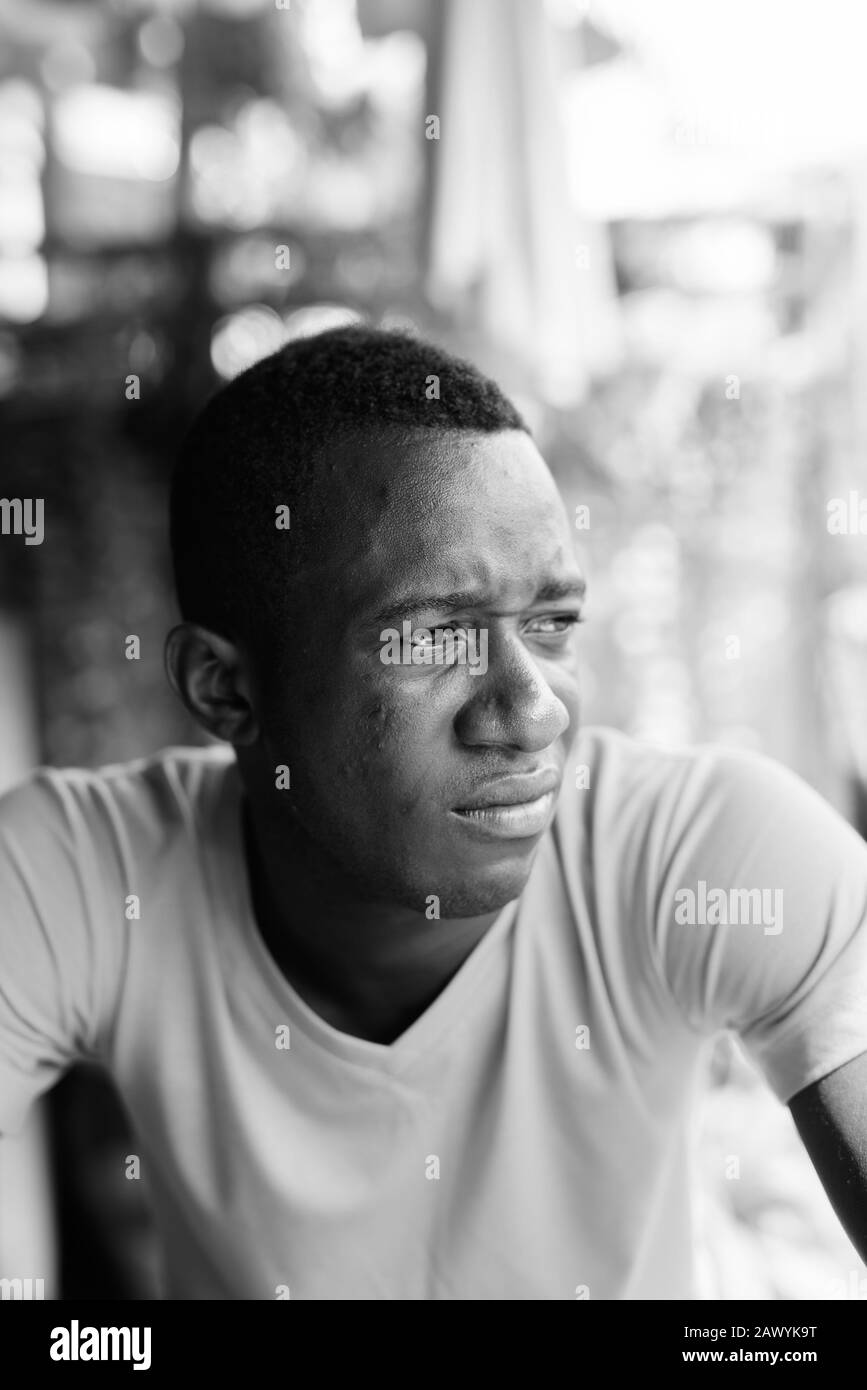 Gesicht der jungen schwarzen afrikanischen Mann zu denken, während der Abstand in den ruhigen Garten im Freien suchen Stockfoto