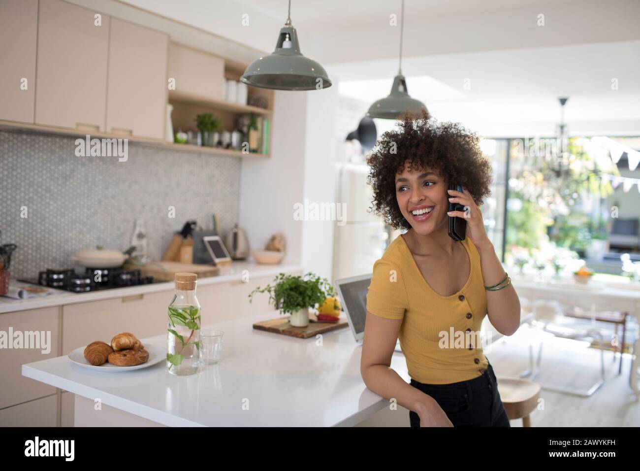 Fröhliche junge Frau, die in der Küche mit dem Smartphone spricht Stockfoto