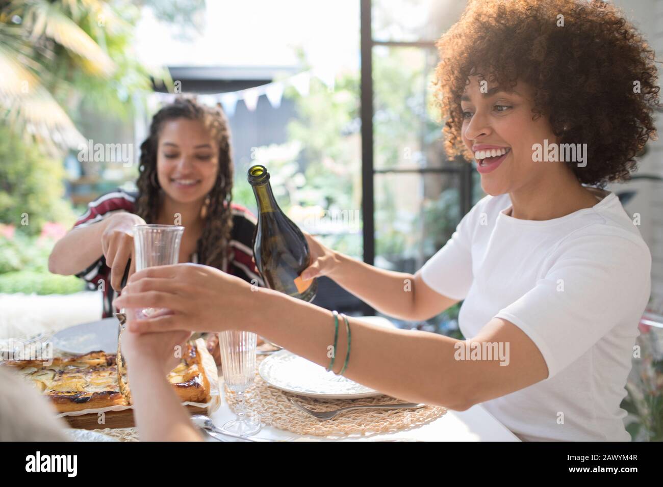 Fröhliche junge Frau, die Wein für einen Freund am Tisch gießt Stockfoto