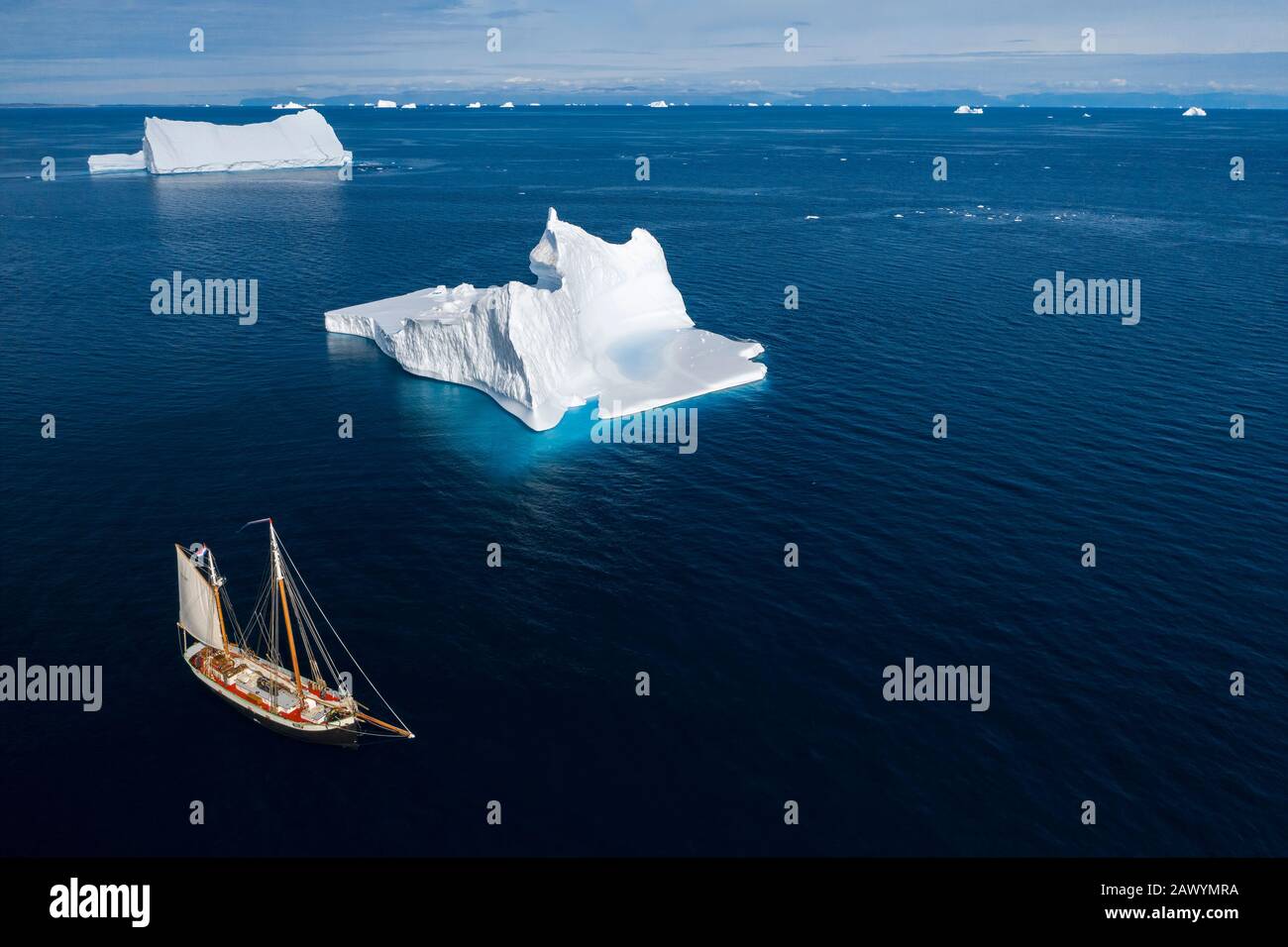 Schiff segelt an Eisbergen auf dem sonnigen blauen Ozean Grönlands vorbei Stockfoto
