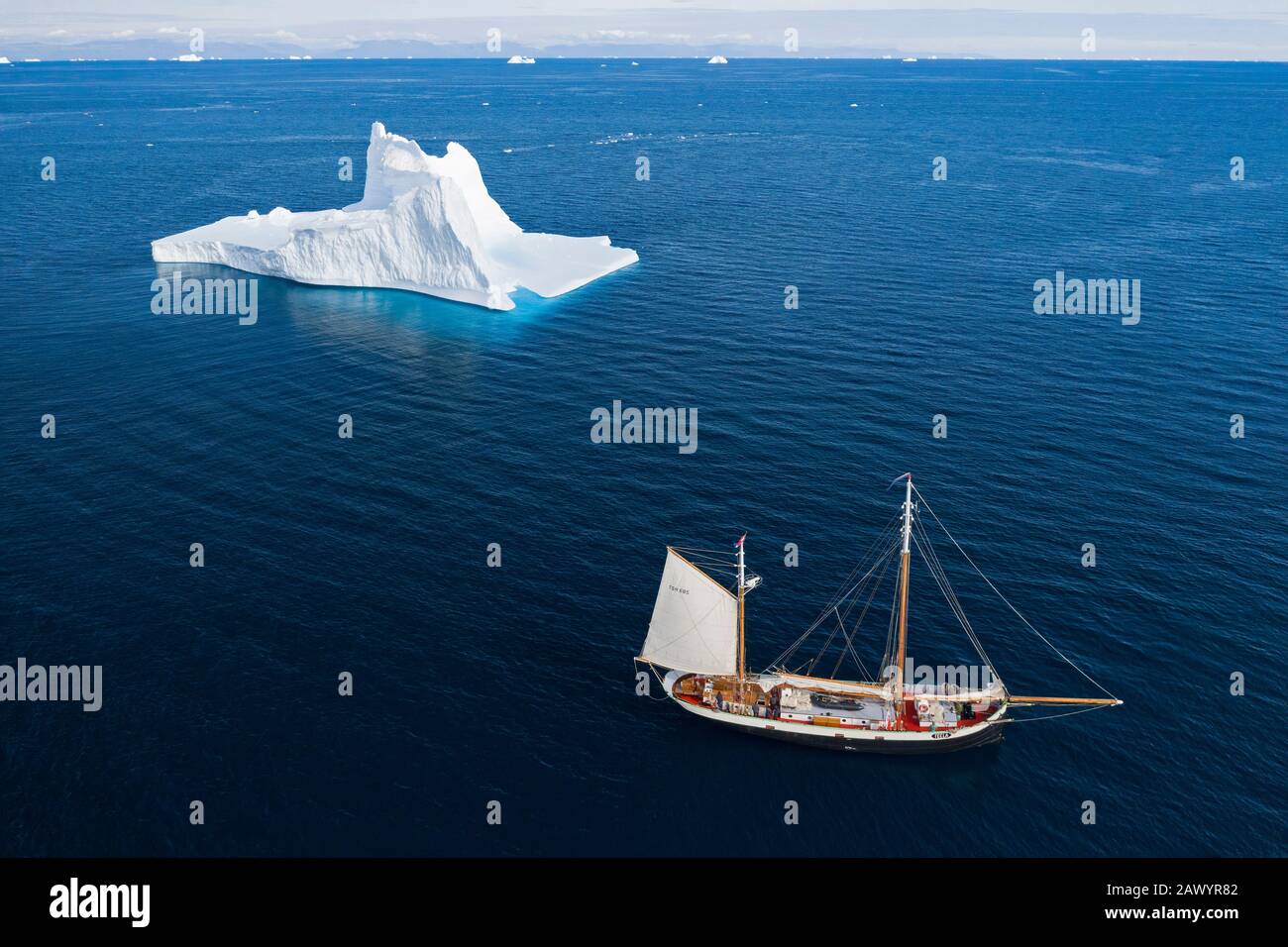 Schiff segelt am majestätischen Eisberg auf dem sonnigen blauen Atlantischen Ozean Grönlands vorbei Stockfoto