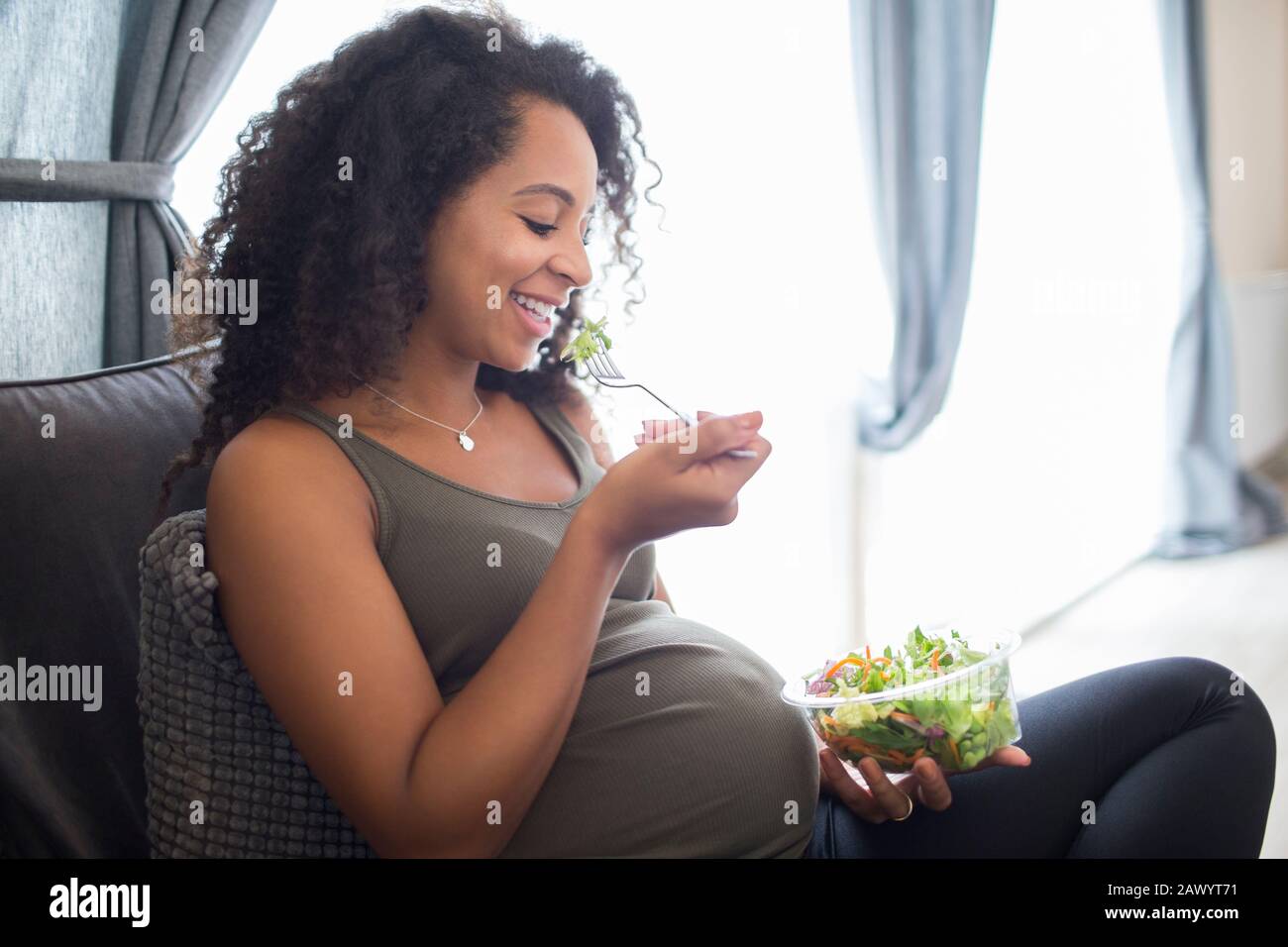 Fröhliche junge schwangere Frau, die Salat isst Stockfoto