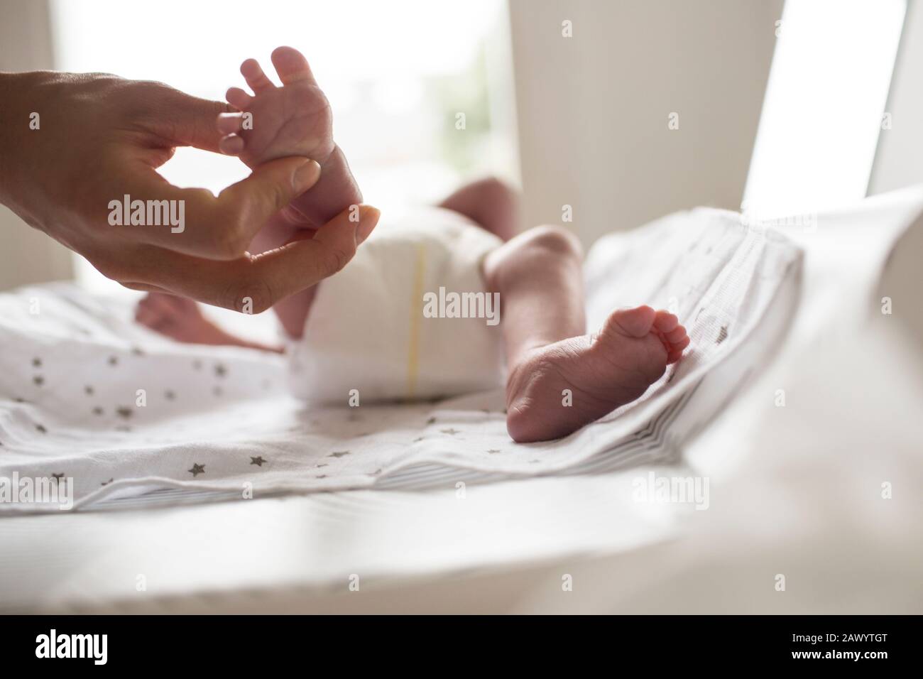 Mutter, die einen kleinen Fuß des neugeborenen Sohnes auf dem Wechseltisch hält Stockfoto