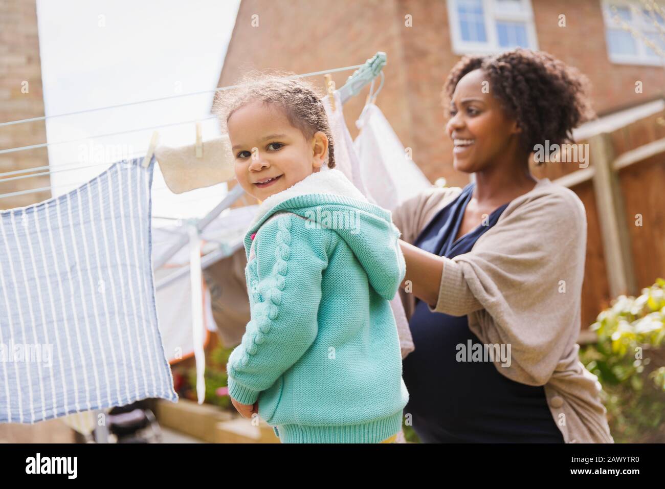 Portrait glückliches Mädchen, das schwangeren Mutter hilft, Wäsche an der Wäscheleine zu hängen Stockfoto