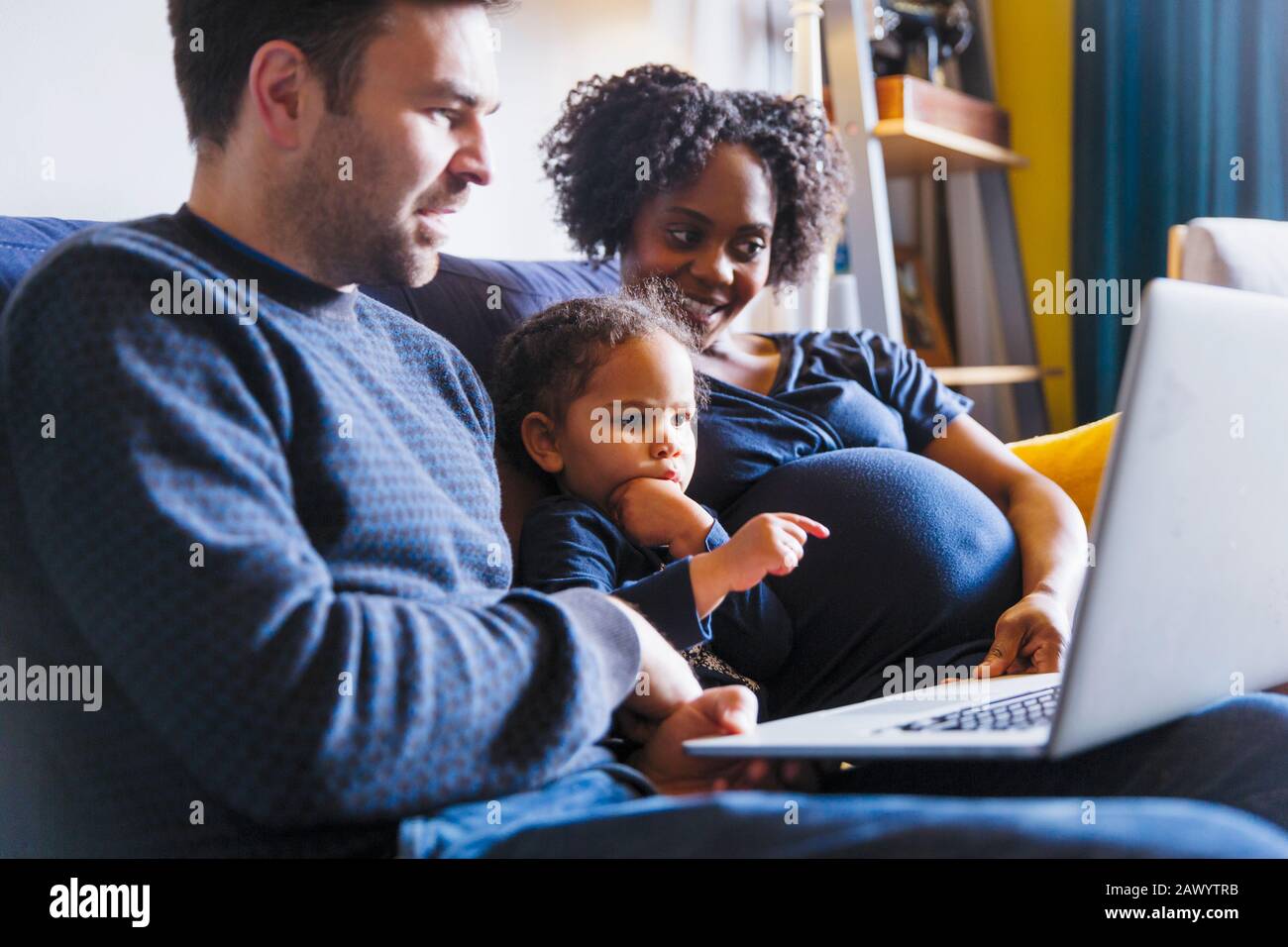 Junge schwangere Familie mit Laptop auf dem Sofa Stockfoto