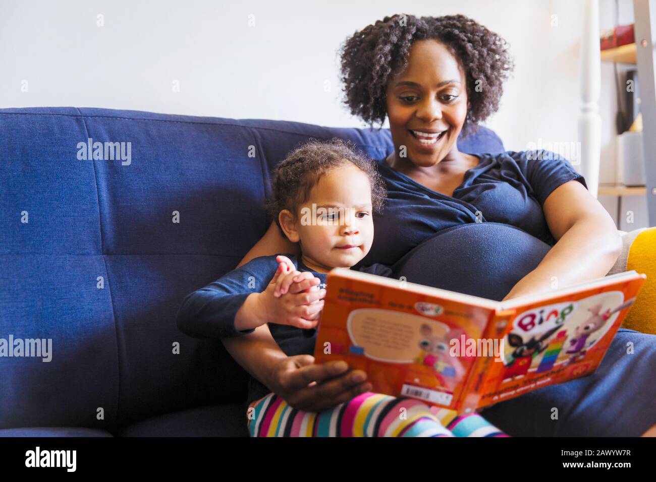 Schwangere Mutter liest Buch zur Tochter auf dem Sofa Stockfoto